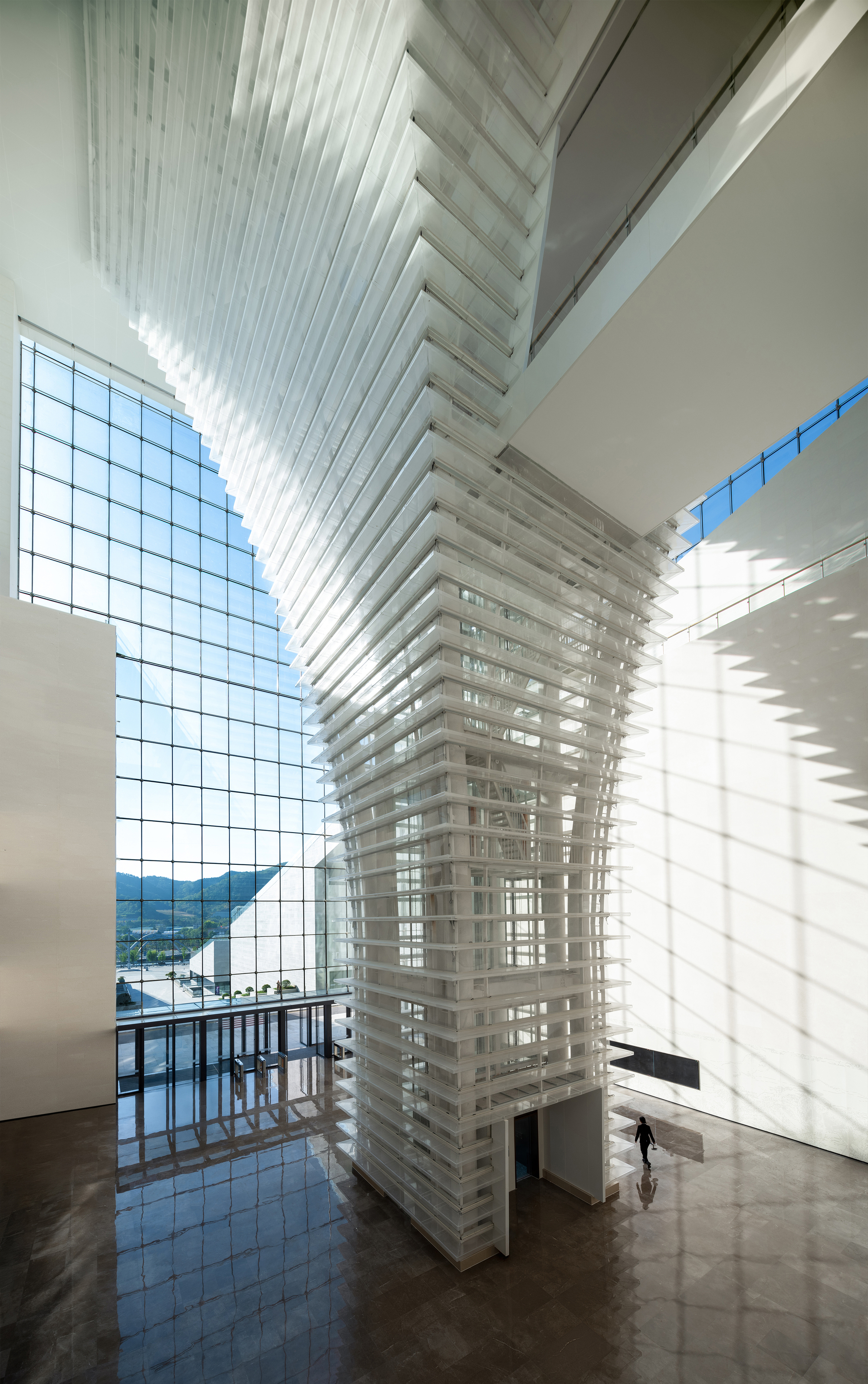Interior atrium with layered horizontal fins and curtain wall framing a single visitor below
