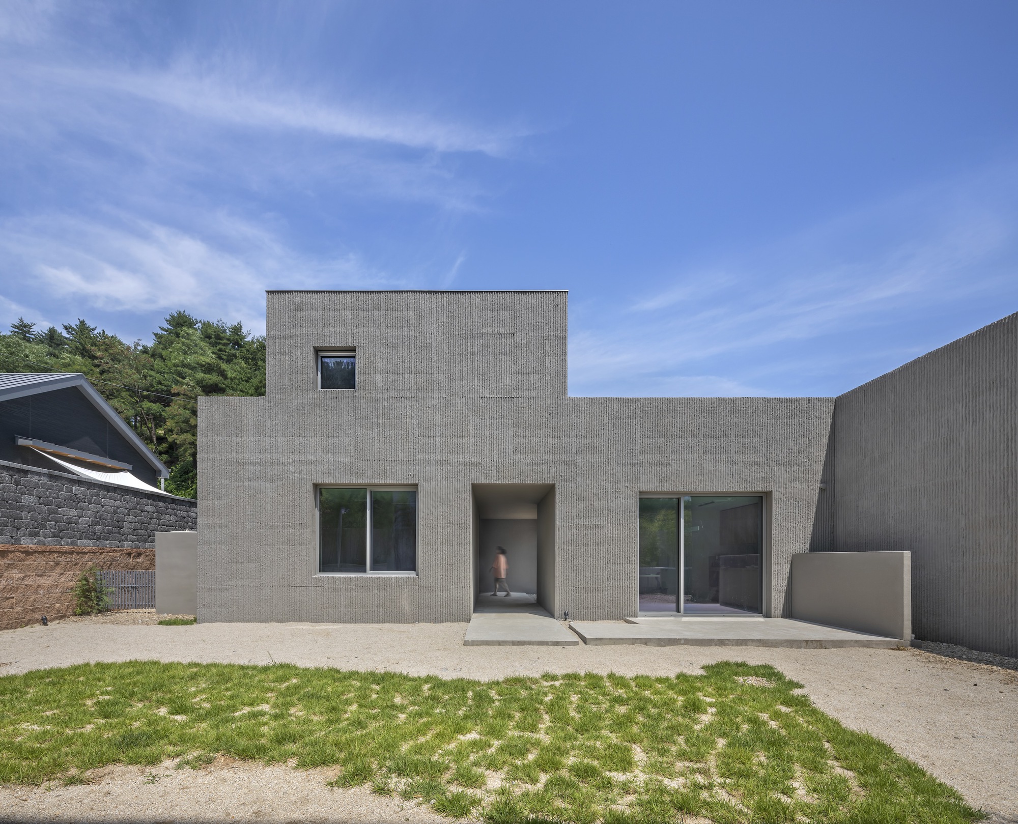 Front facade of concrete block residence with recessed entry and grass courtyard under clear skies