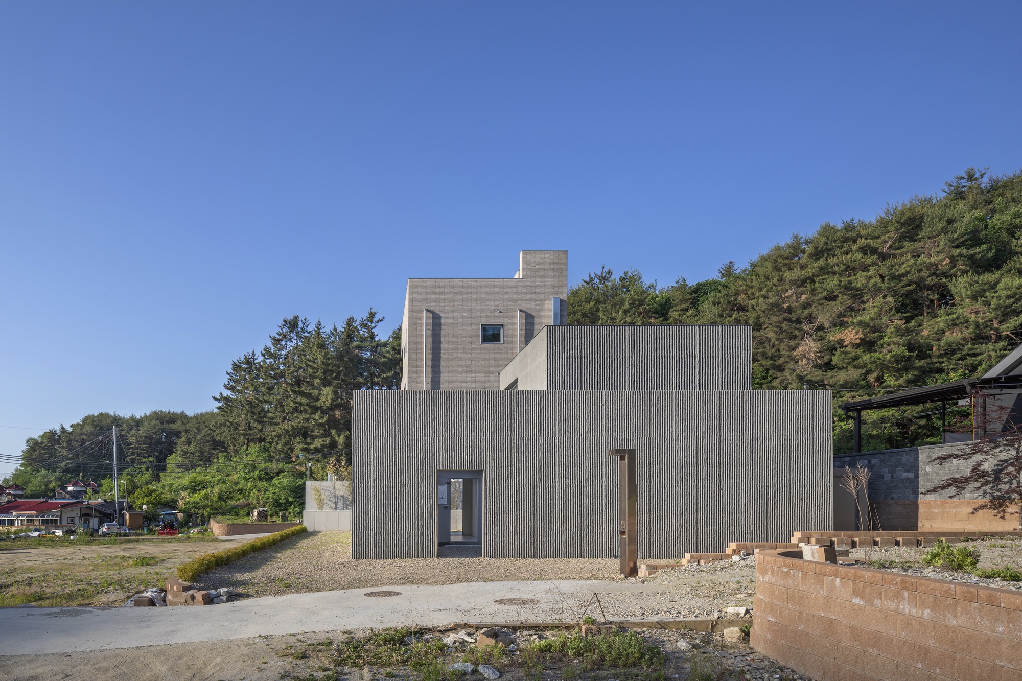 Stacked concrete block volumes with narrow windows set into a hillside along a gravel drive
