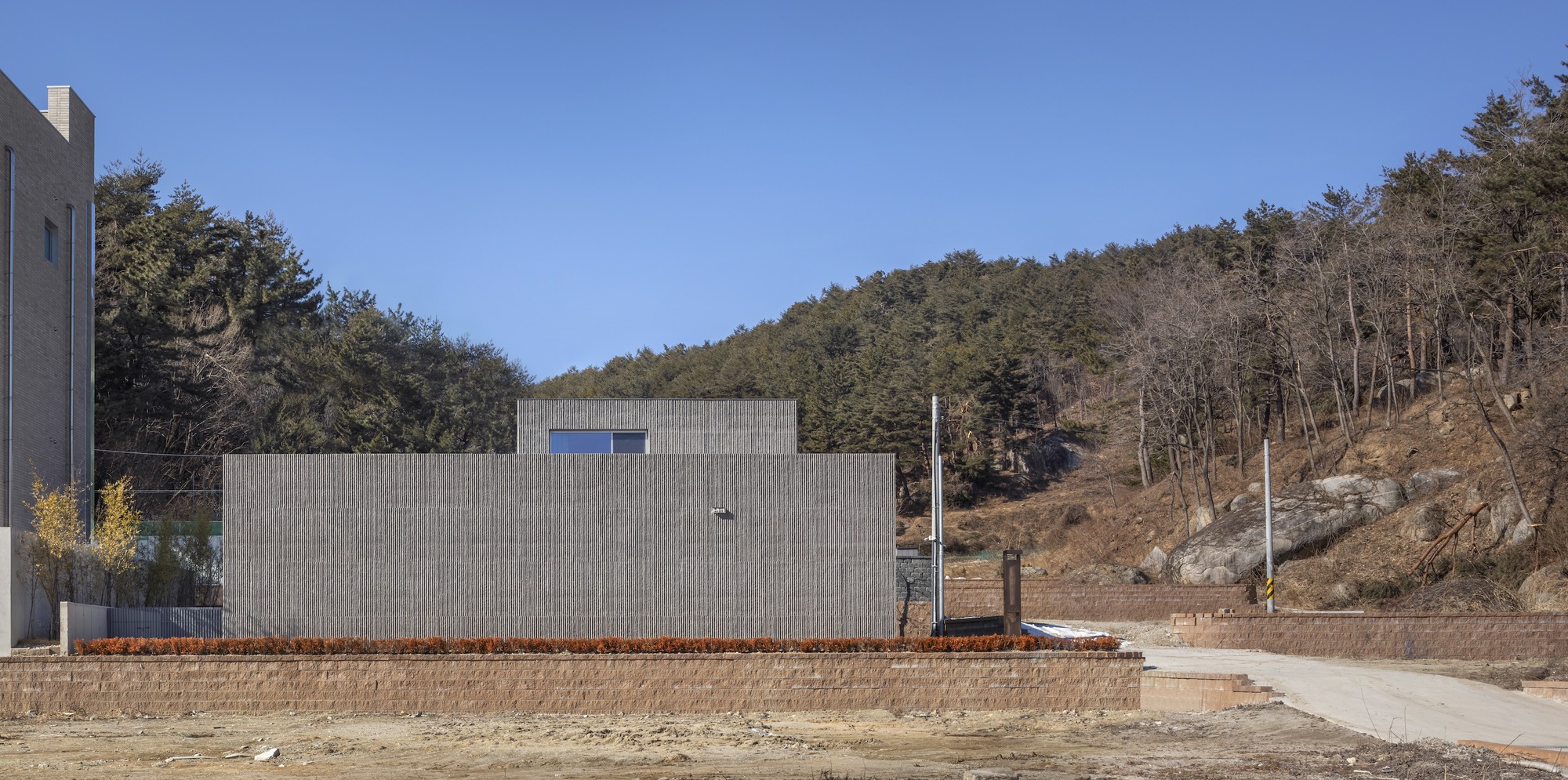 Rear elevation of the concrete block wall facing a hillside road during winter or early spring