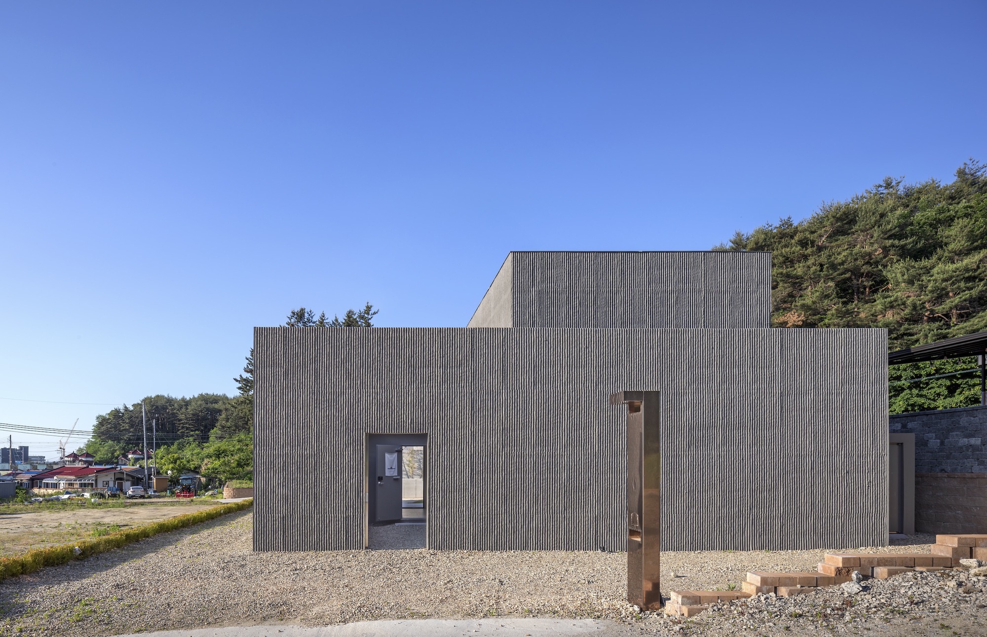 Corrugated metal facade with stepped volumes and a central glazed entry on gravel ground