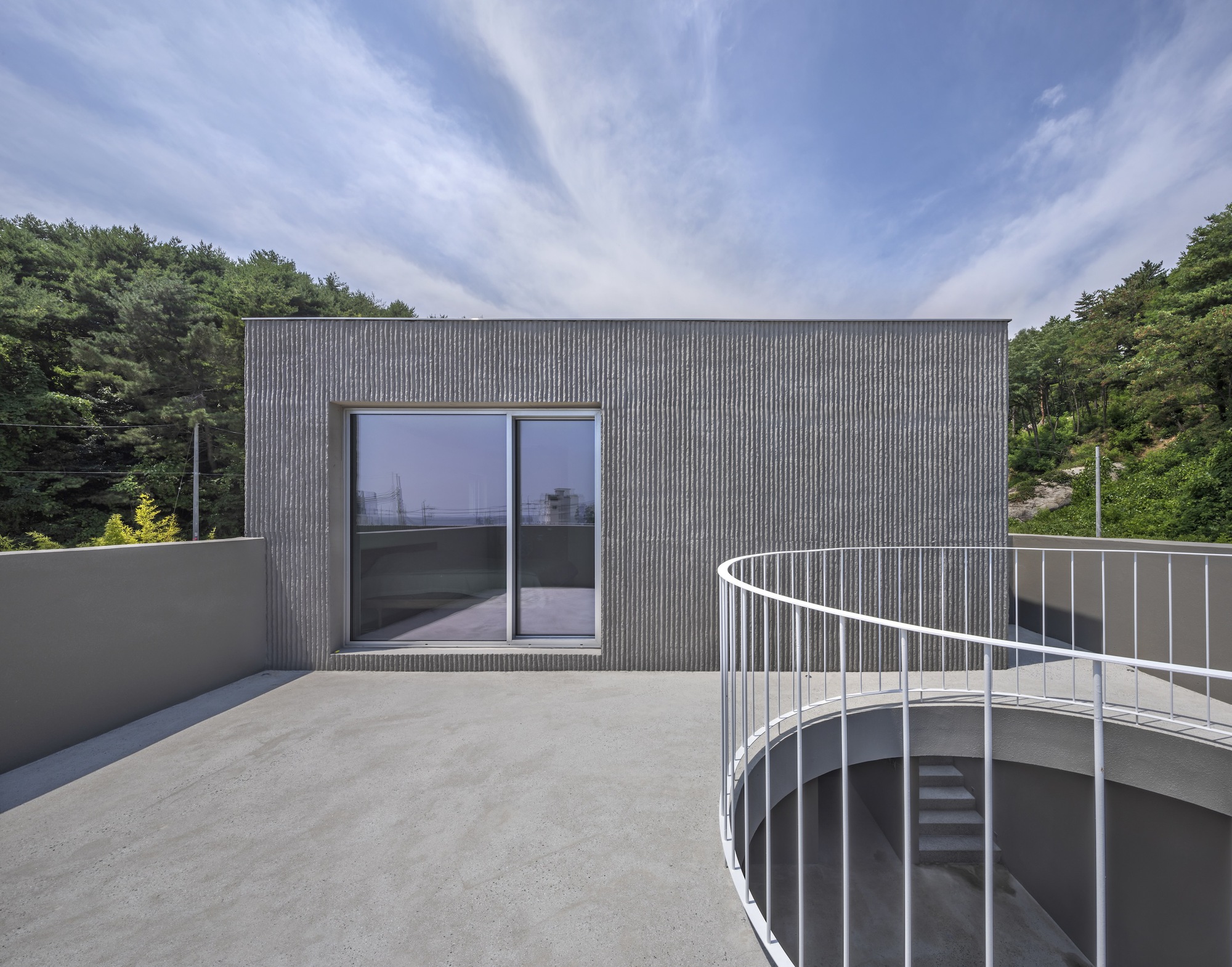 Rooftop terrace with curved metal railing and sliding glass doors against ribbed cladding