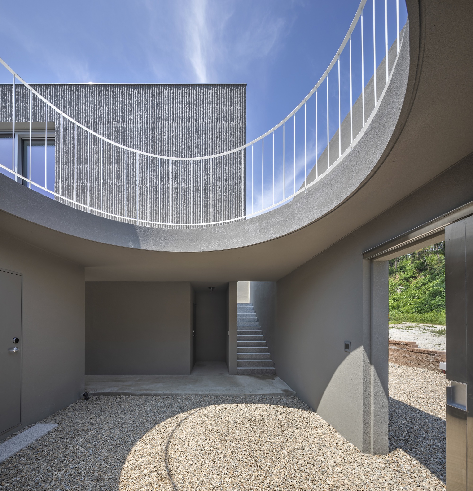 Circular courtyard open to sky with curved railing above and gravel floor below