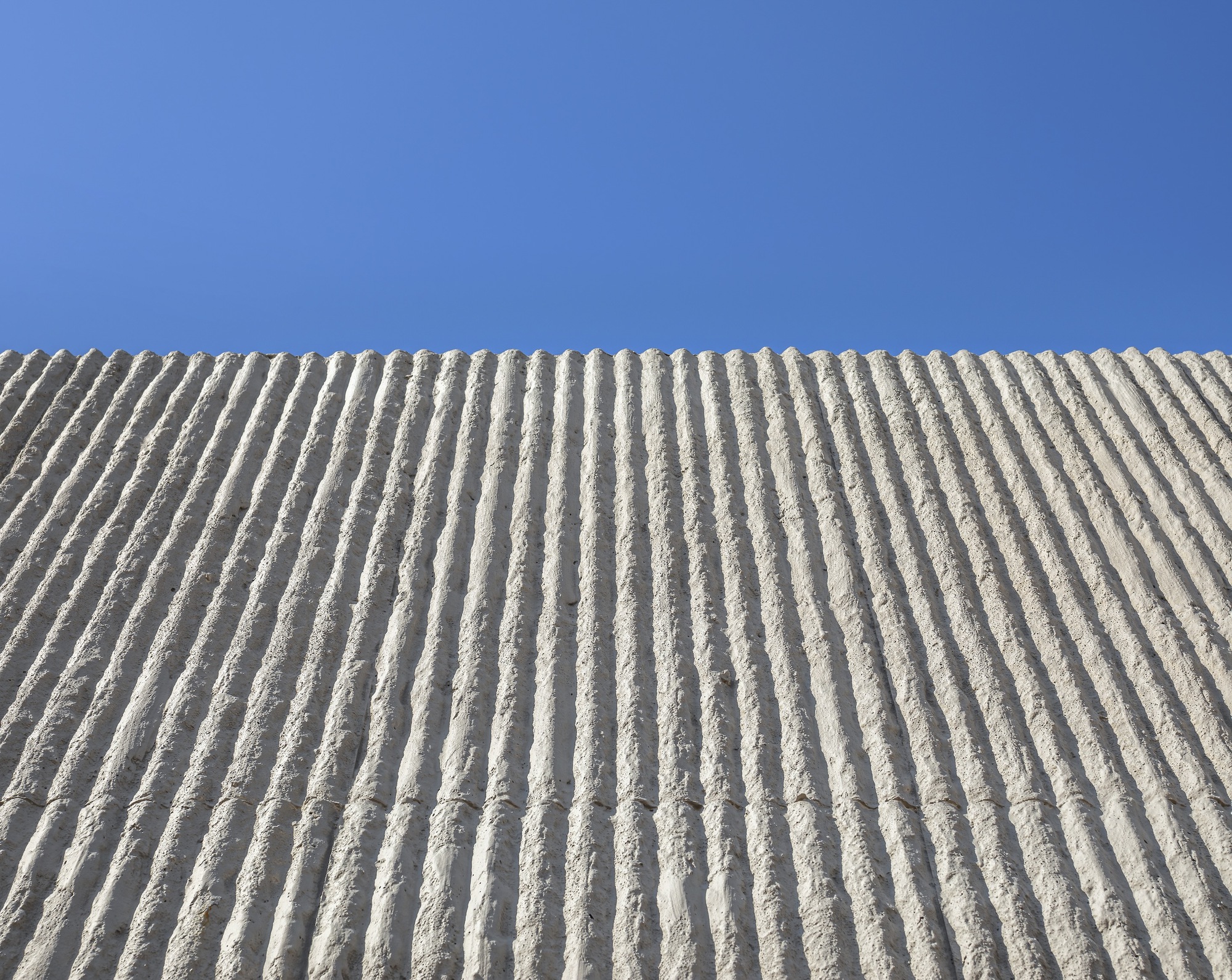 Upward view of ribbed concrete wall surface against a clear blue sky
