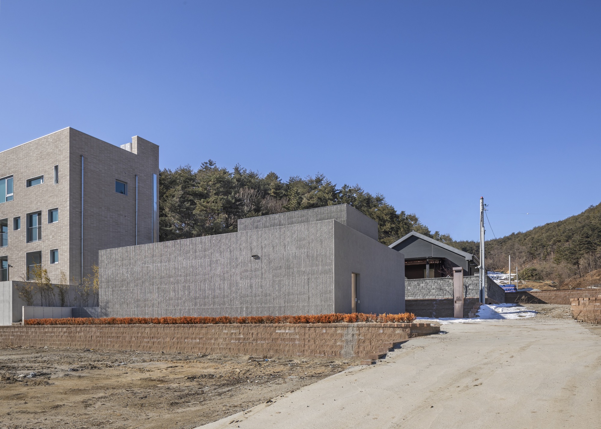 Street view of vertically ribbed concrete volume with timber planters along the base in winter