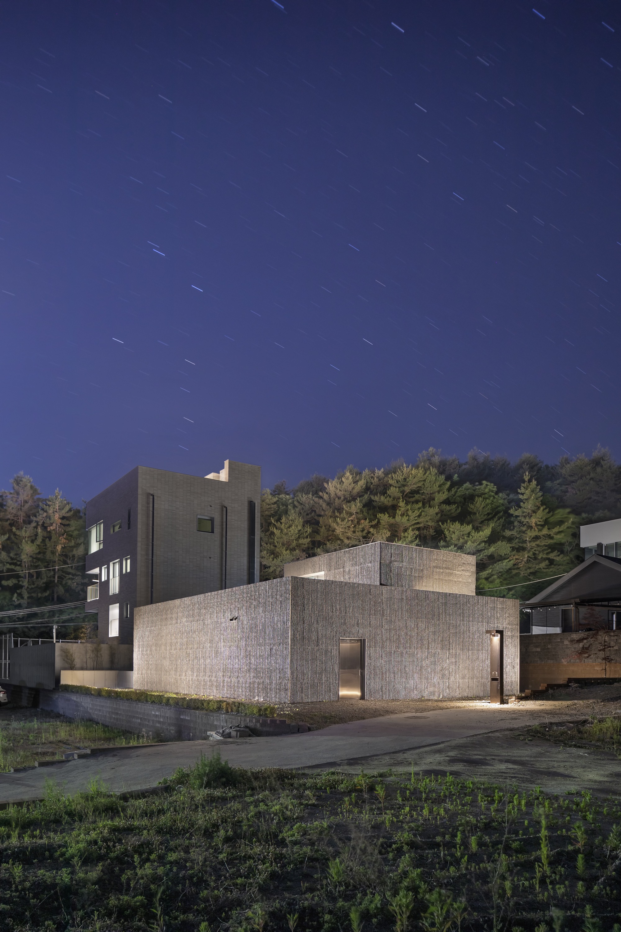 Textured concrete volumes with corner windows photographed under star trails at twilight