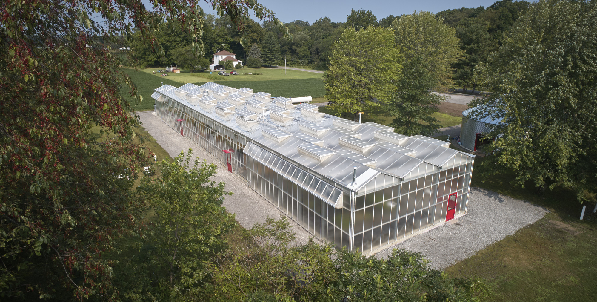 Aerial view of the greenhouse with translucent polycarbonate cladding and sawtooth roof surrounded by trees and lawn