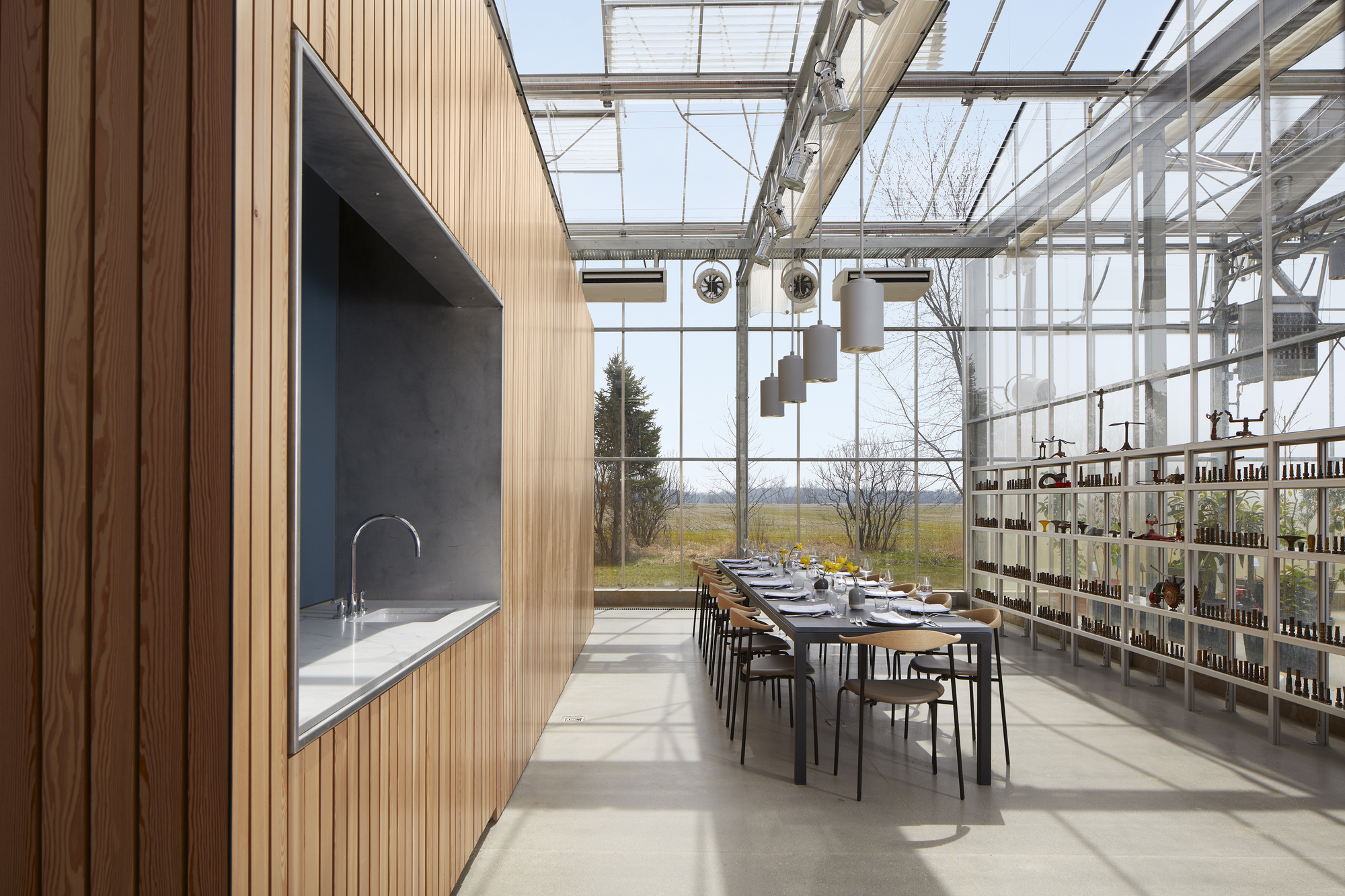 Dining area with long table set for a meal beneath the glazed roof with views to winter fields