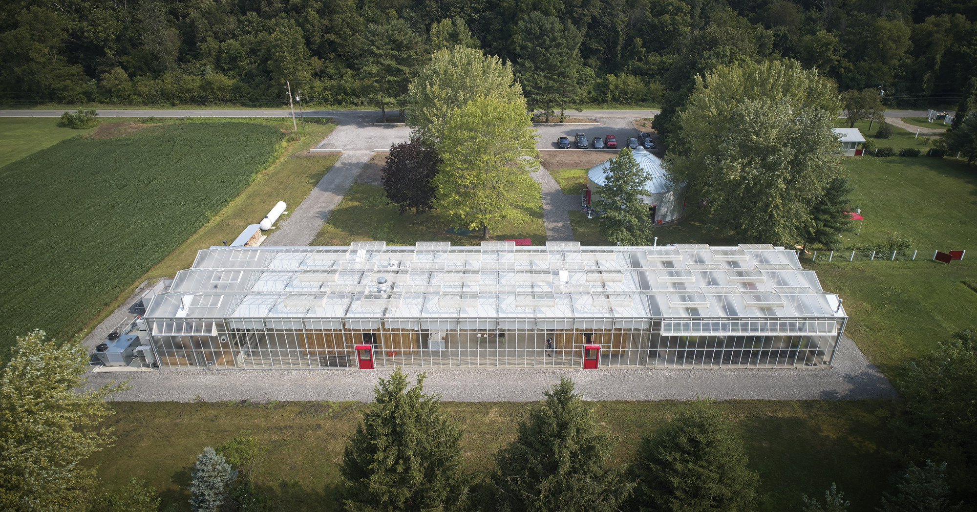 Aerial view of the rectangular greenhouse roof with gridded polycarbonate panels framed by parking and summer trees