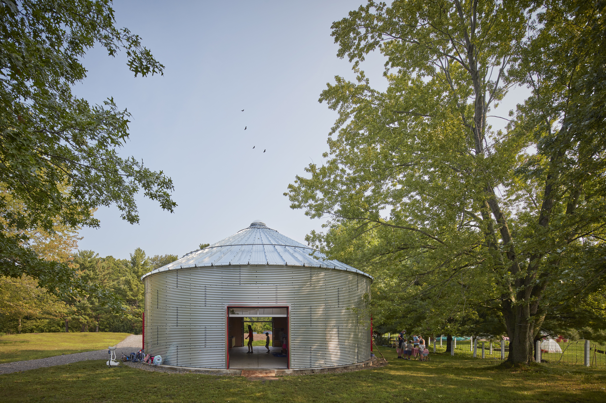 Corrugated metal grain silo repurposed with large red sliding doors opening to views of the surrounding lawn
