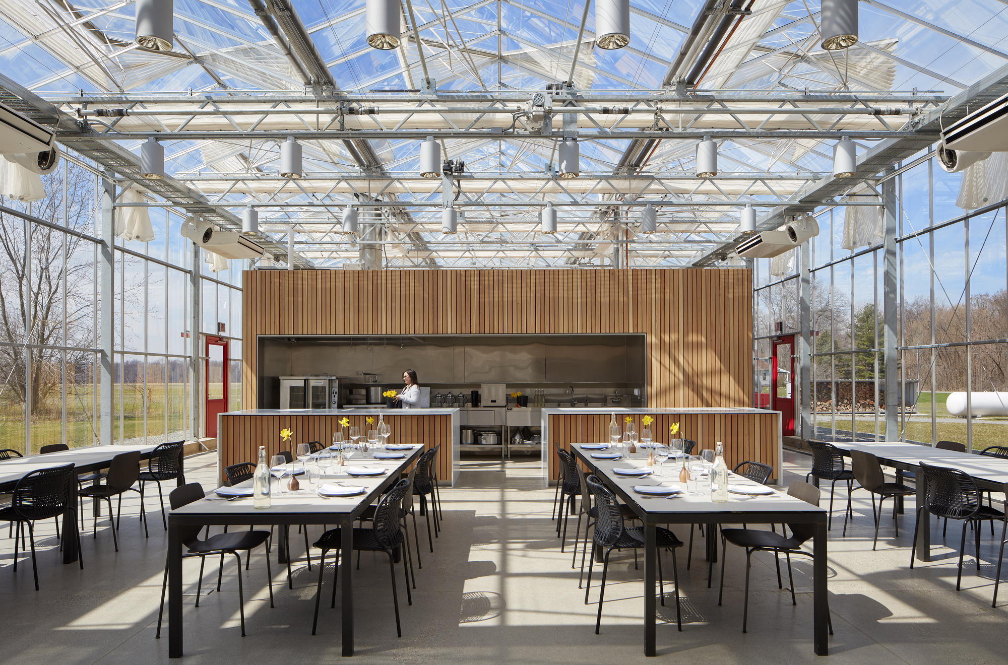 Dining space under an exposed steel truss and glass roof with vertical wood-clad service core