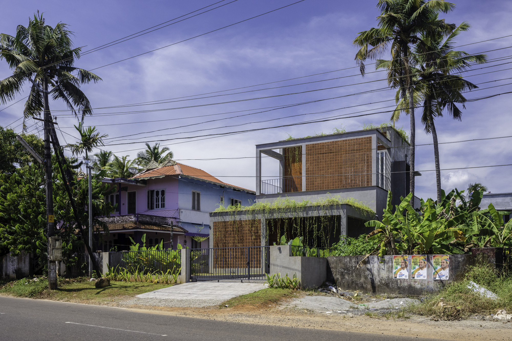 Two-story volume with bamboo screening and cascading greenery set behind a metal gate along a residential street