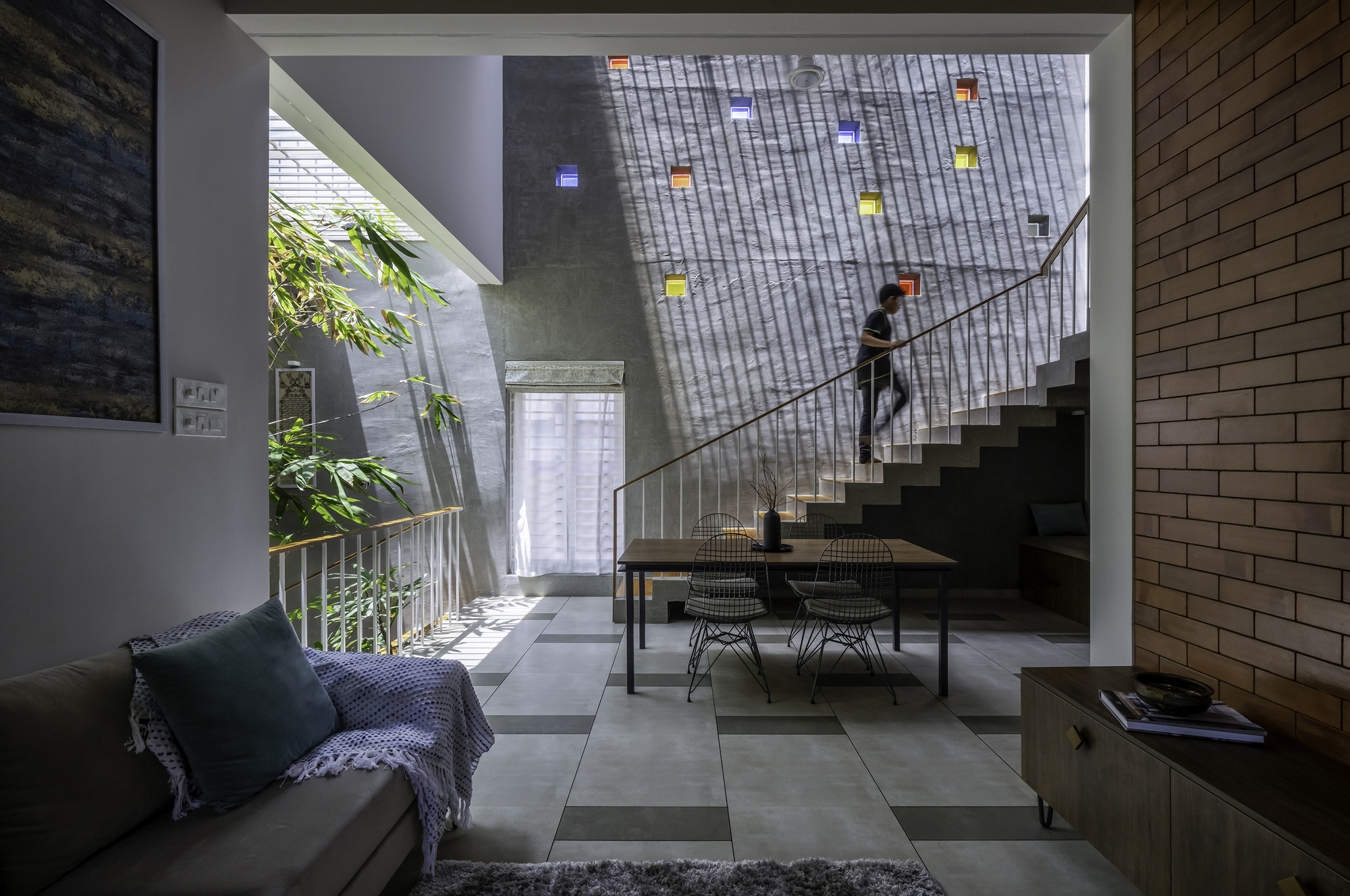 Double-height dining space with concrete stair and perforated brick wall filtering daylight from above