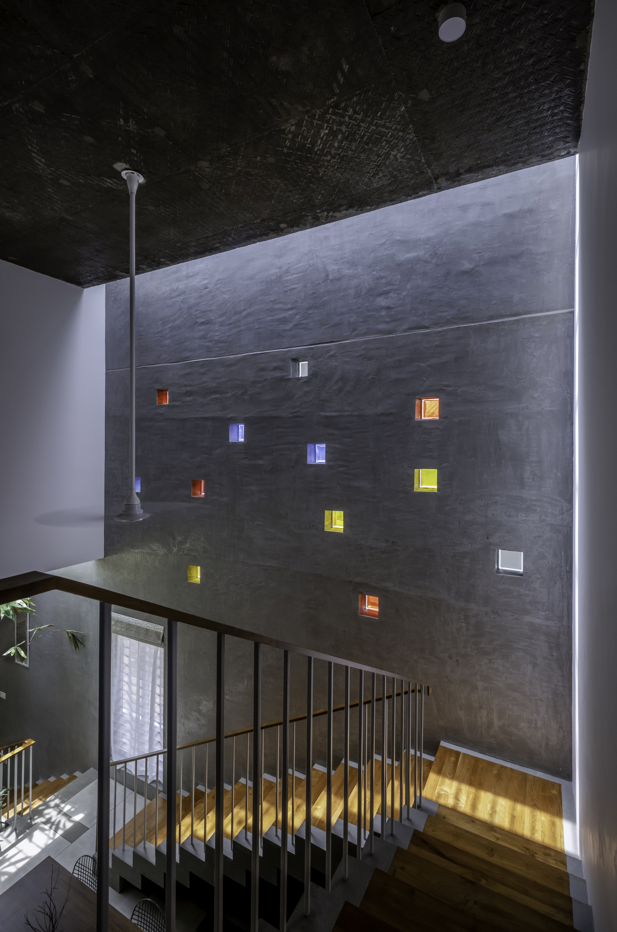 Tall concrete wall with scattered colored glass block inserts beside a metal-railed staircase