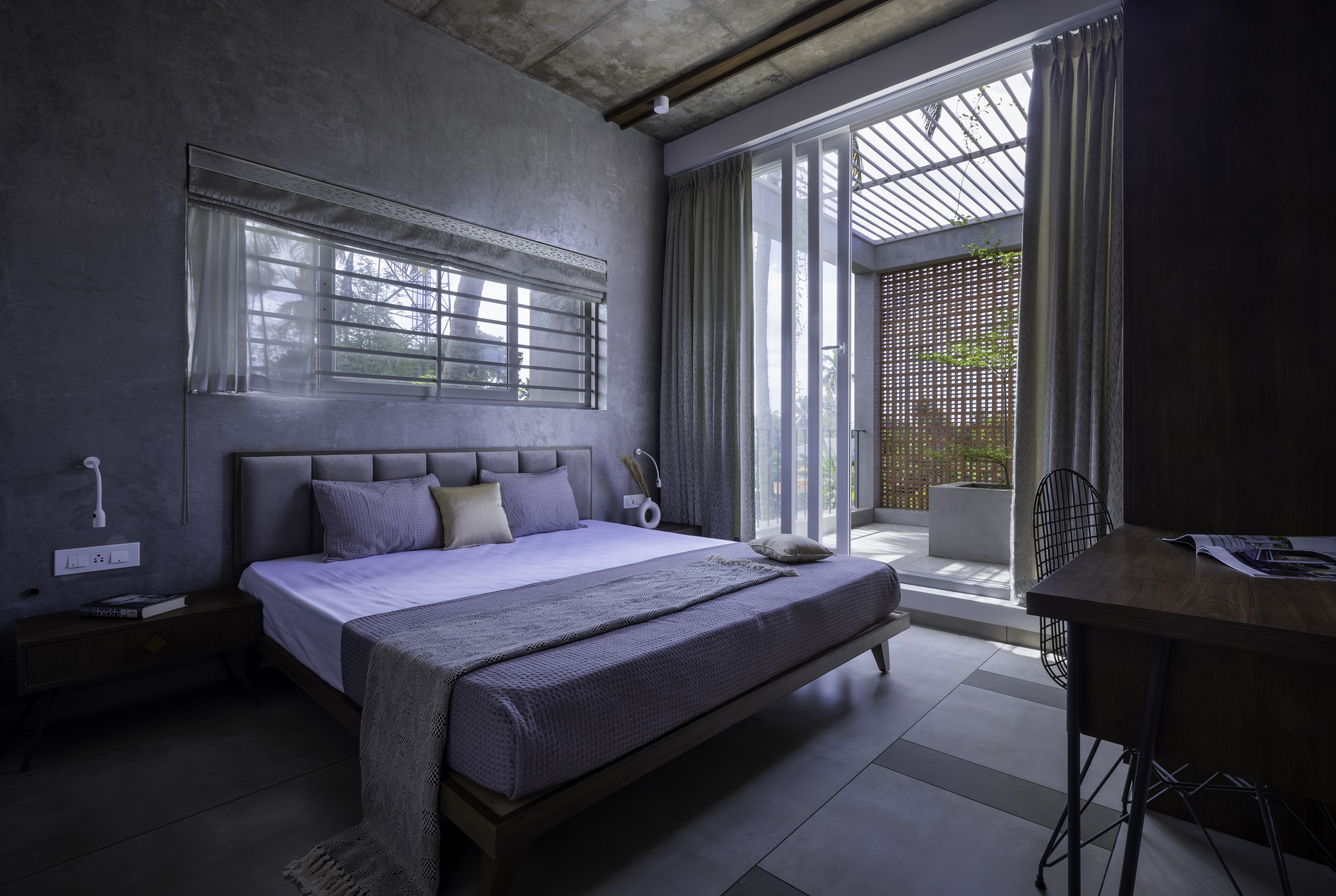Bedroom with exposed concrete ceiling and view through curtained doors to a slatted terrace screen