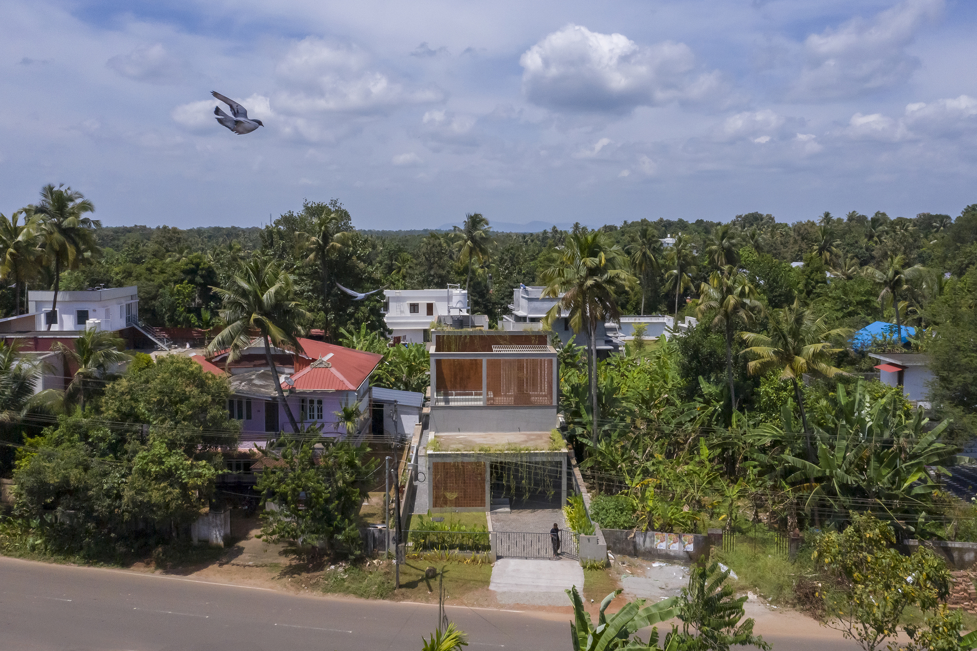 Aerial view of a residence with timber screens among palm trees and neighboring rooftops