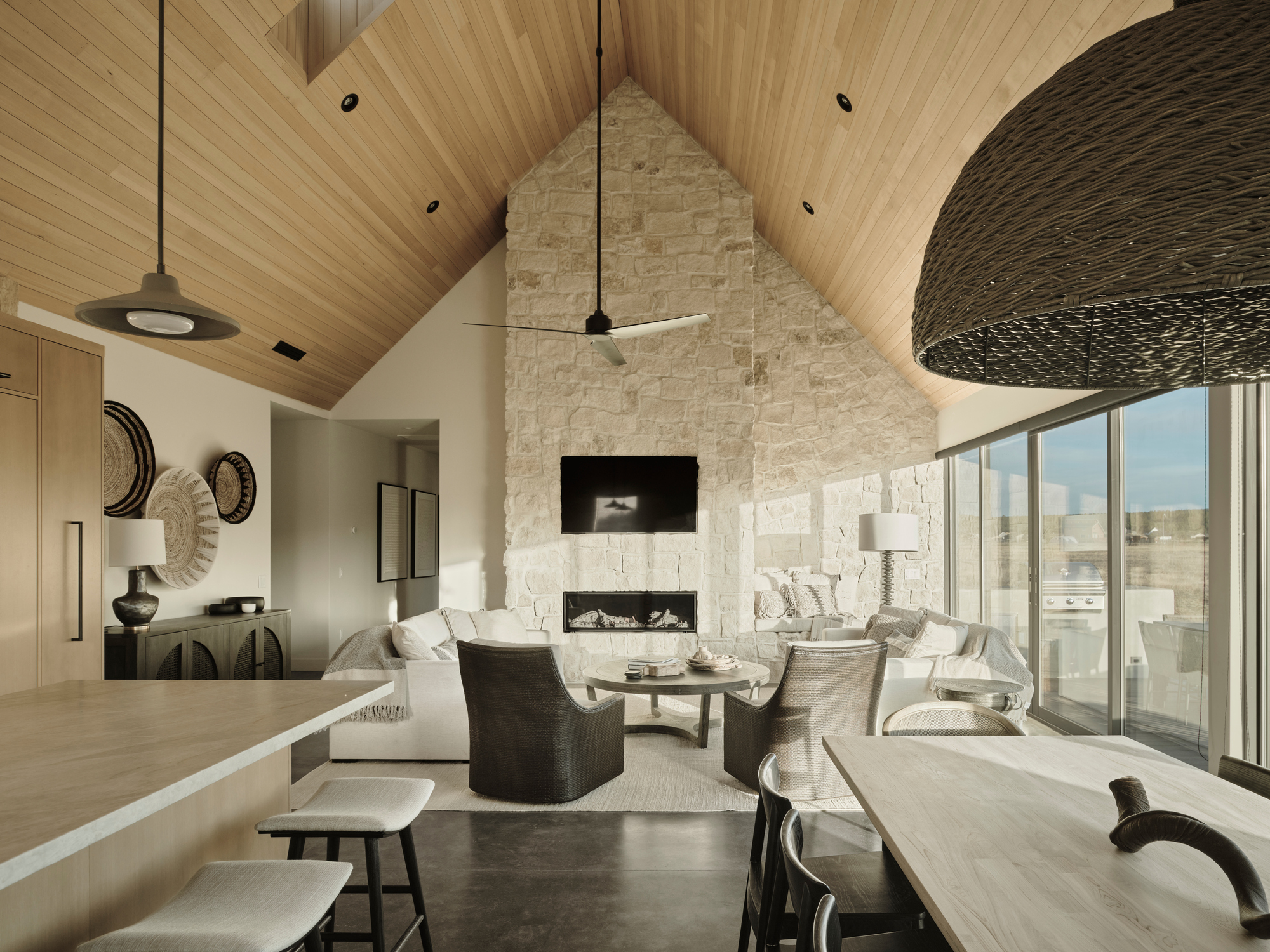Living room with vaulted timber ceiling and stone fireplace wall under pendant fixtures