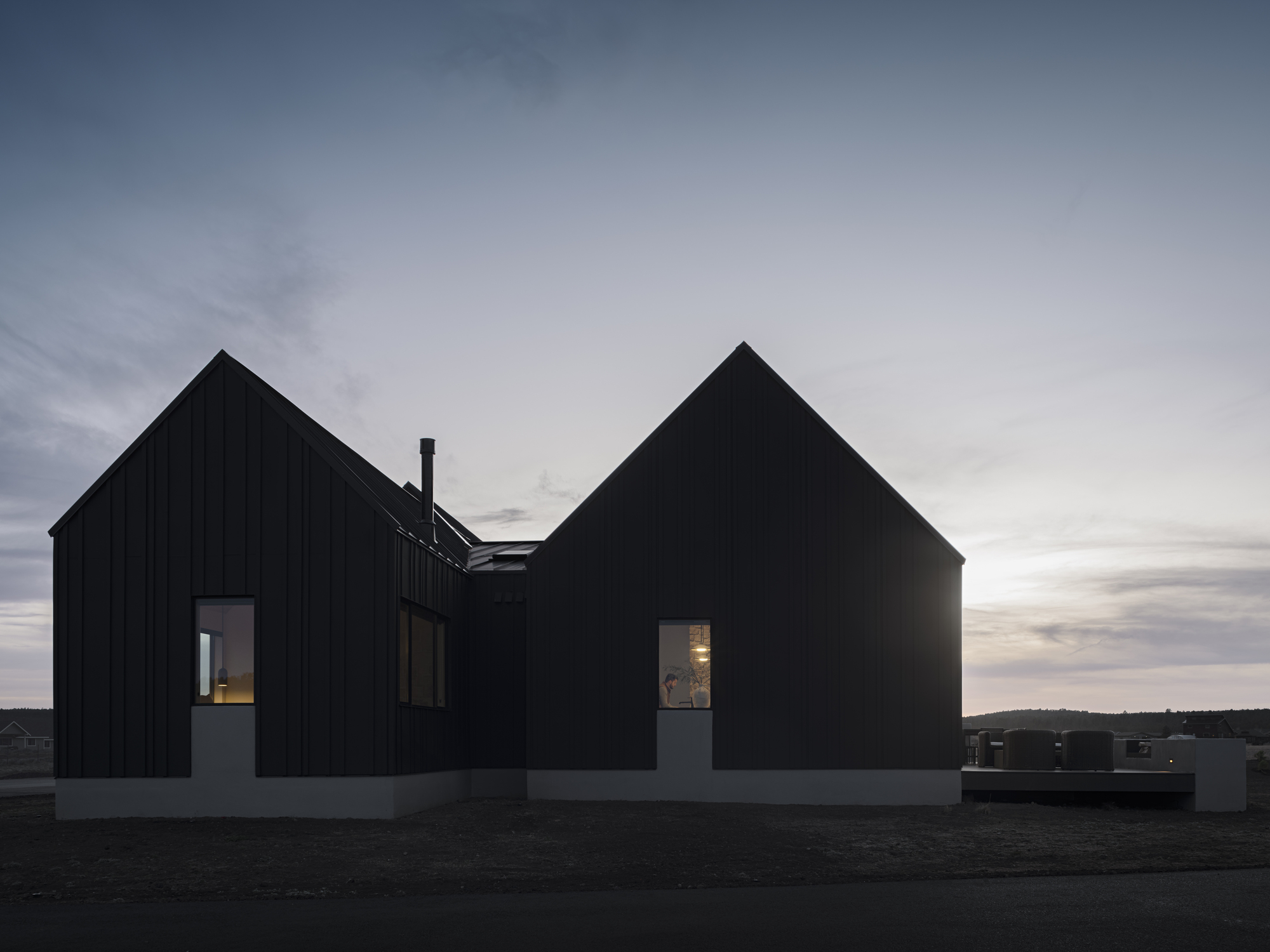 Two gabled volumes with vertical black cladding silhouetted against the dusk sky