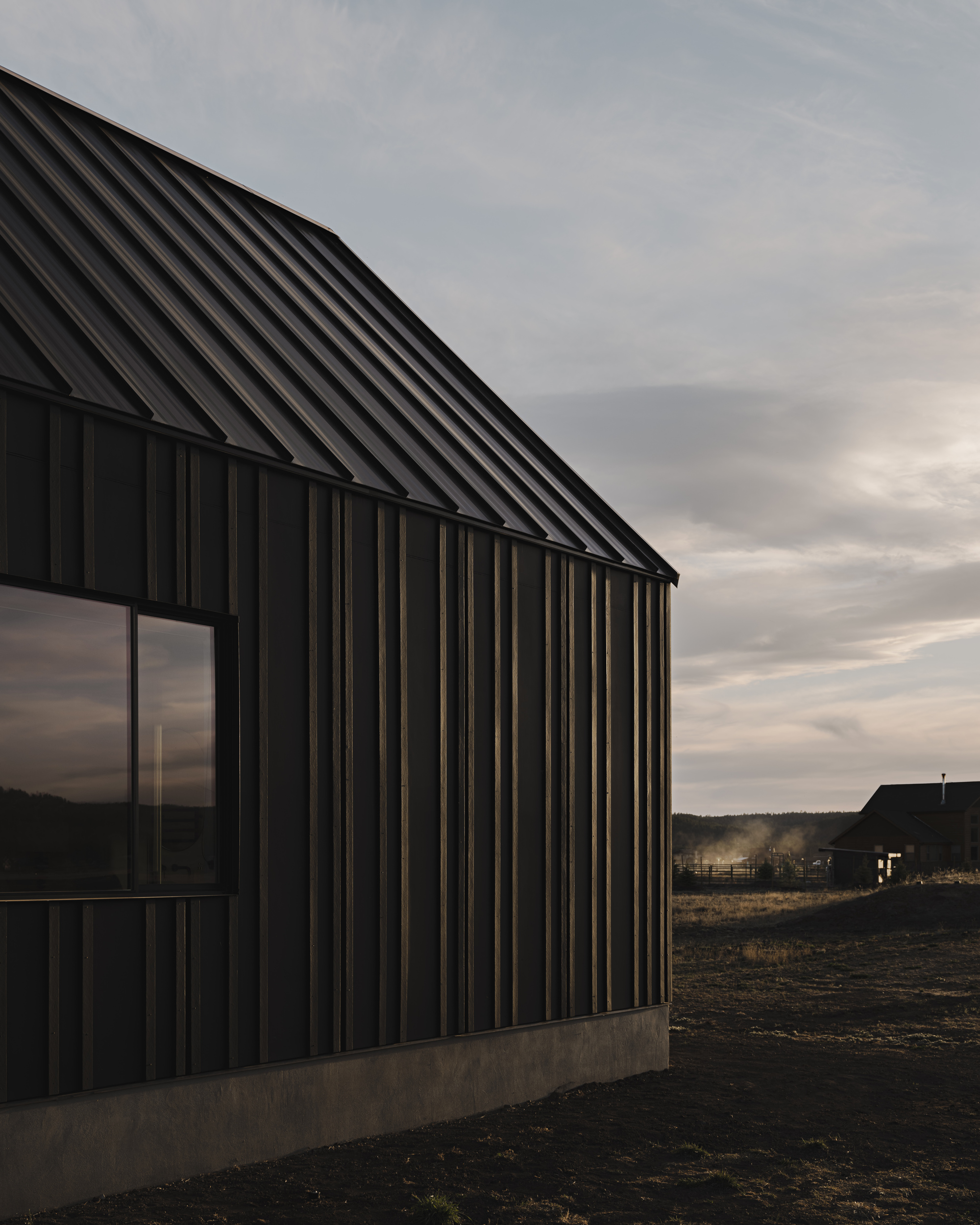Corner detail of black vertical metal cladding meeting the concrete base at twilight
