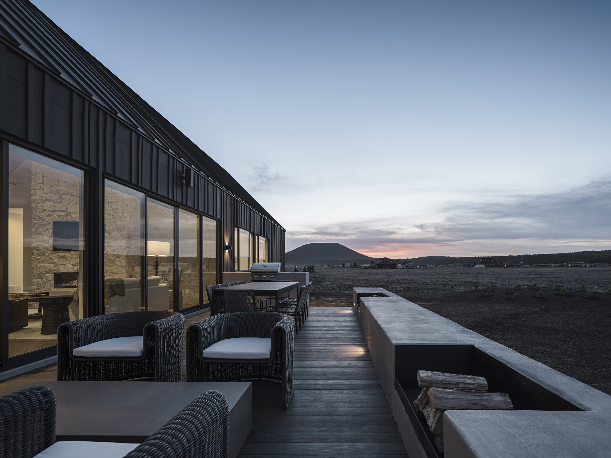 Timber deck terrace with wicker seating and fire pit facing distant hills at sunset