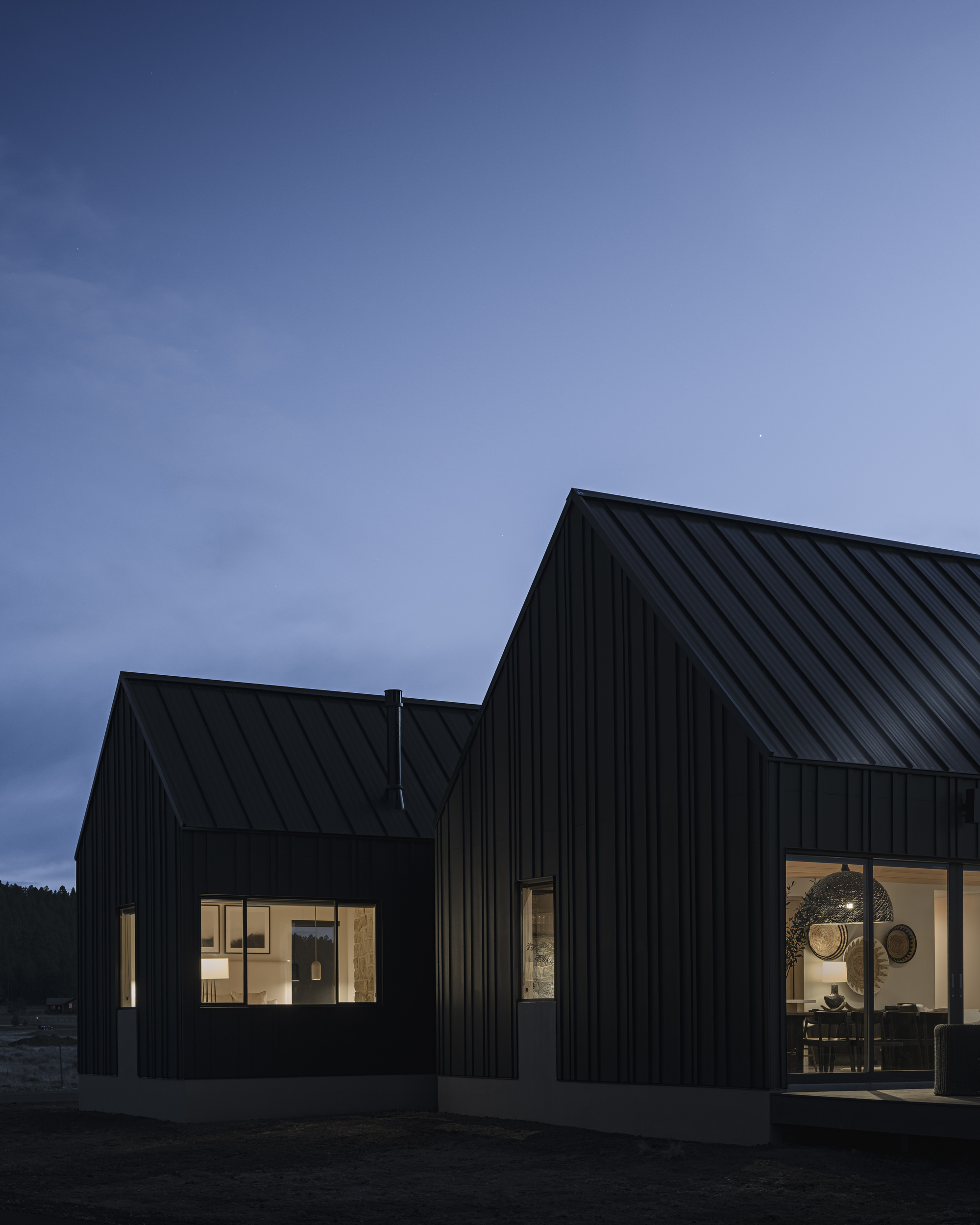 Adjoining gabled volumes with black metal cladding and lit windows under blue evening sky