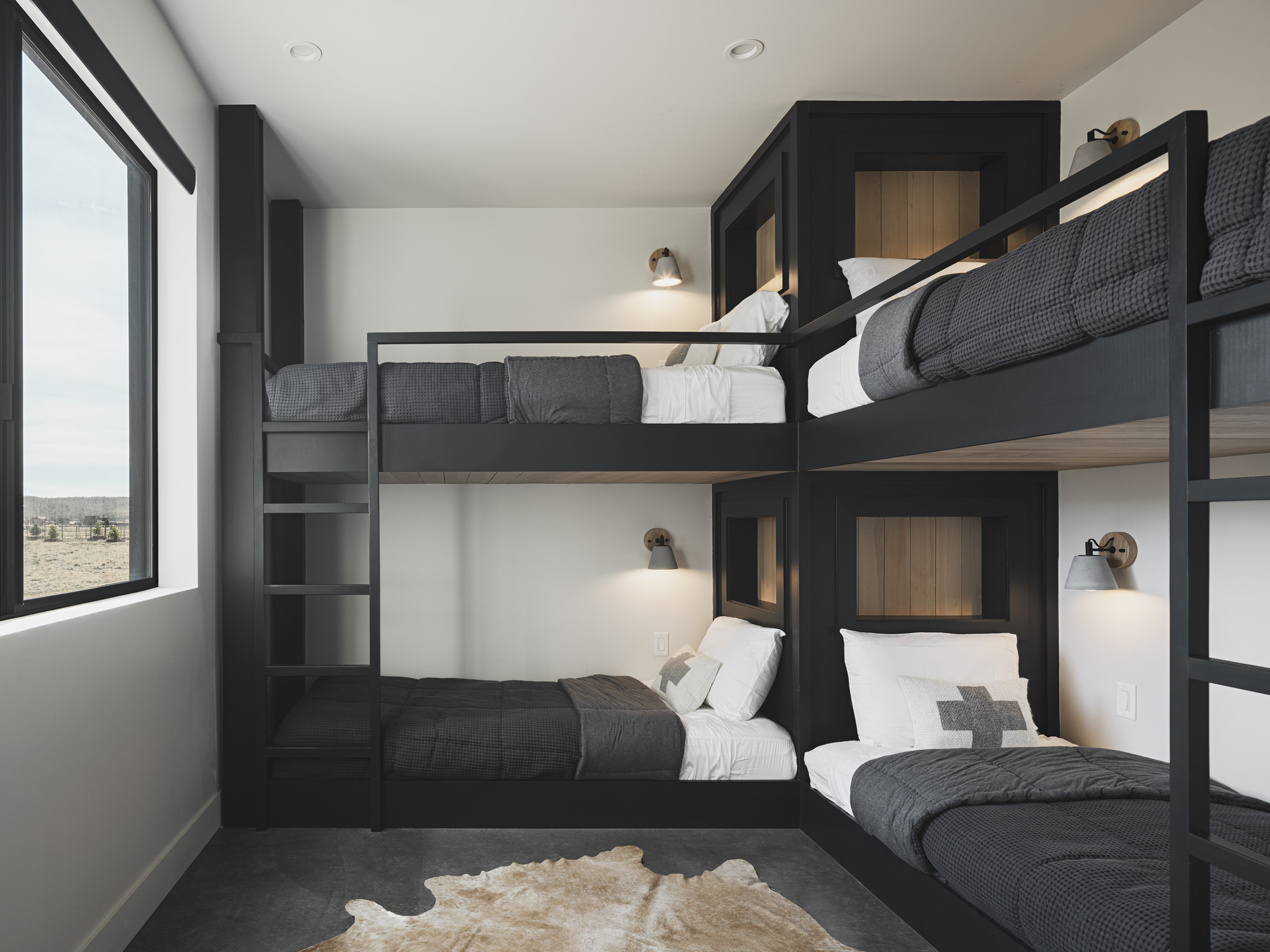 Bunk room with black steel frames and built-in ladders beneath a large window overlooking desert terrain