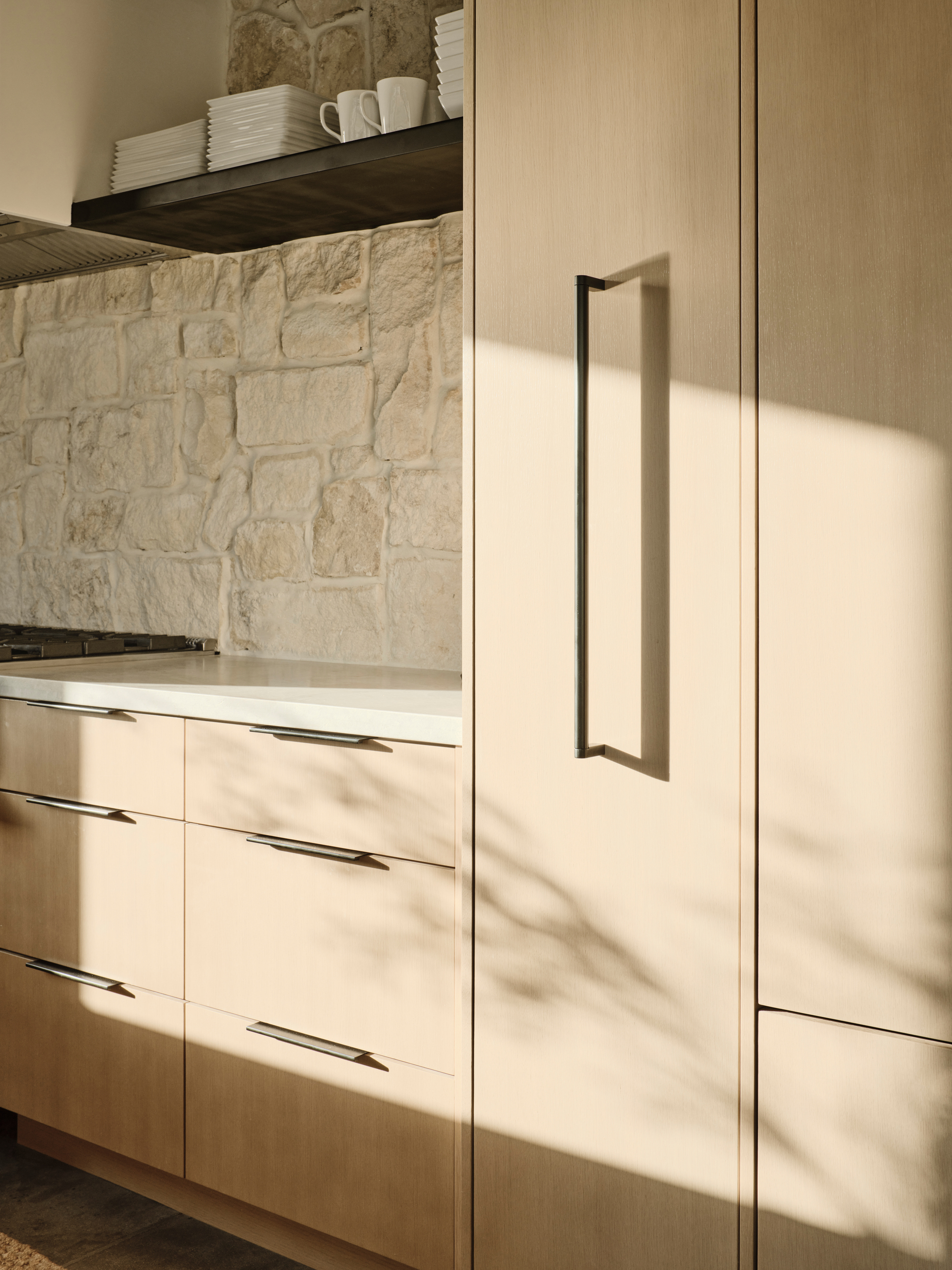 Close-up of light wood cabinetry with vertical bar pulls in afternoon sunlight