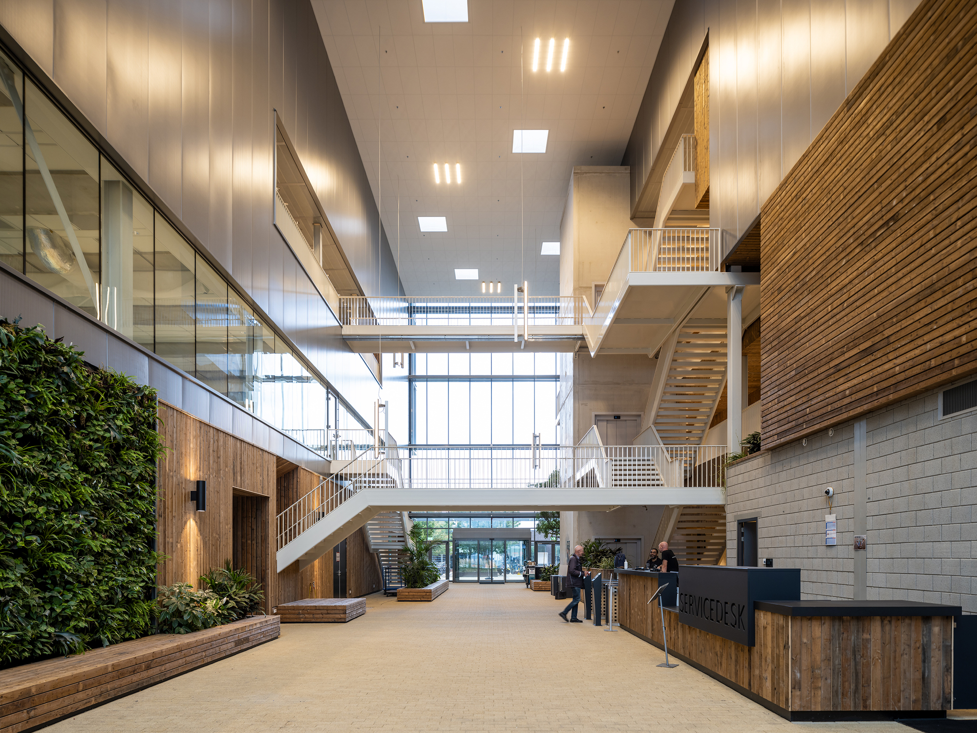 Interior atrium with timber-clad staircases, planted walls, and multiple connecting bridges