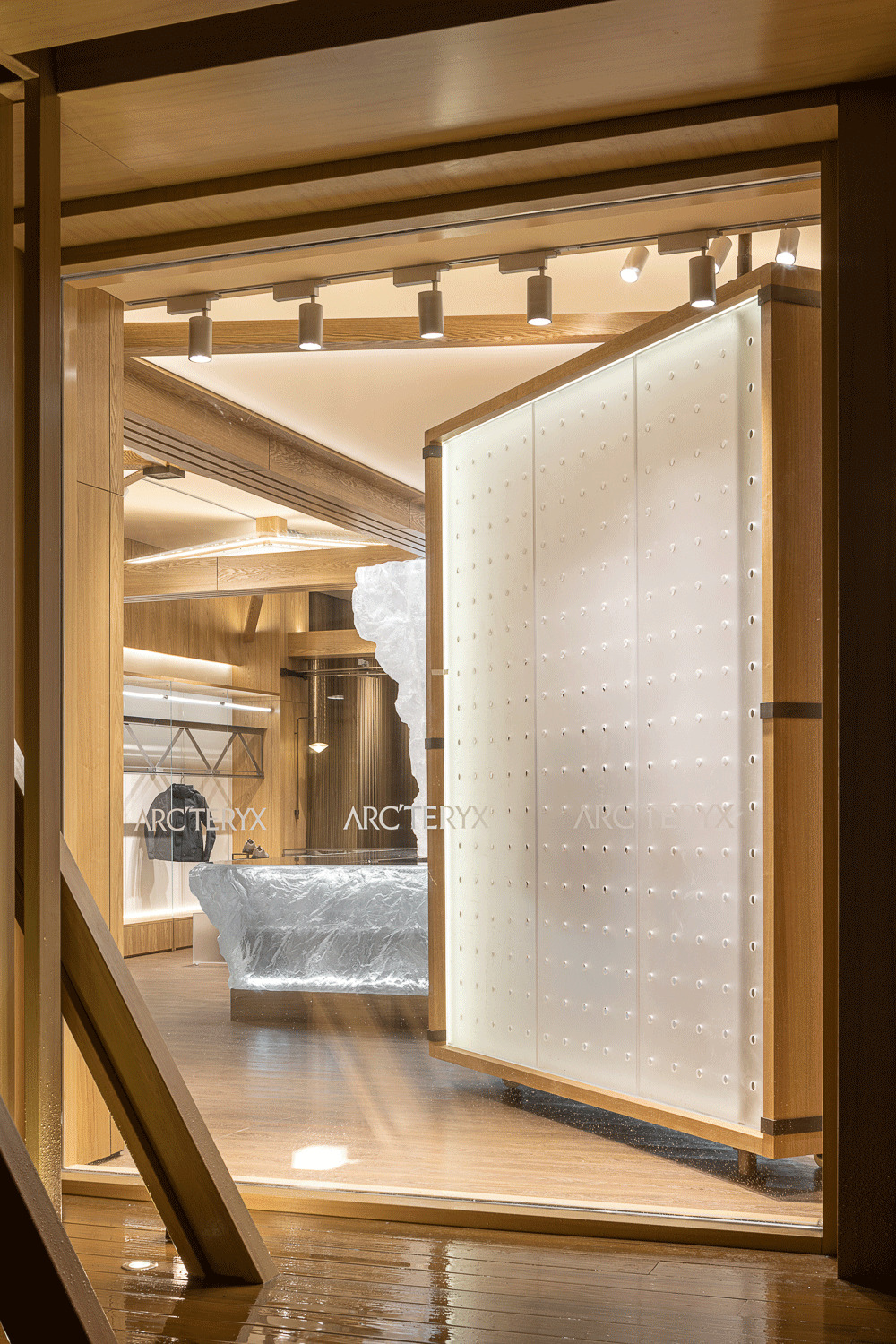 View through timber-framed doorway toward reception desk and pivoting white panel with bronze studs