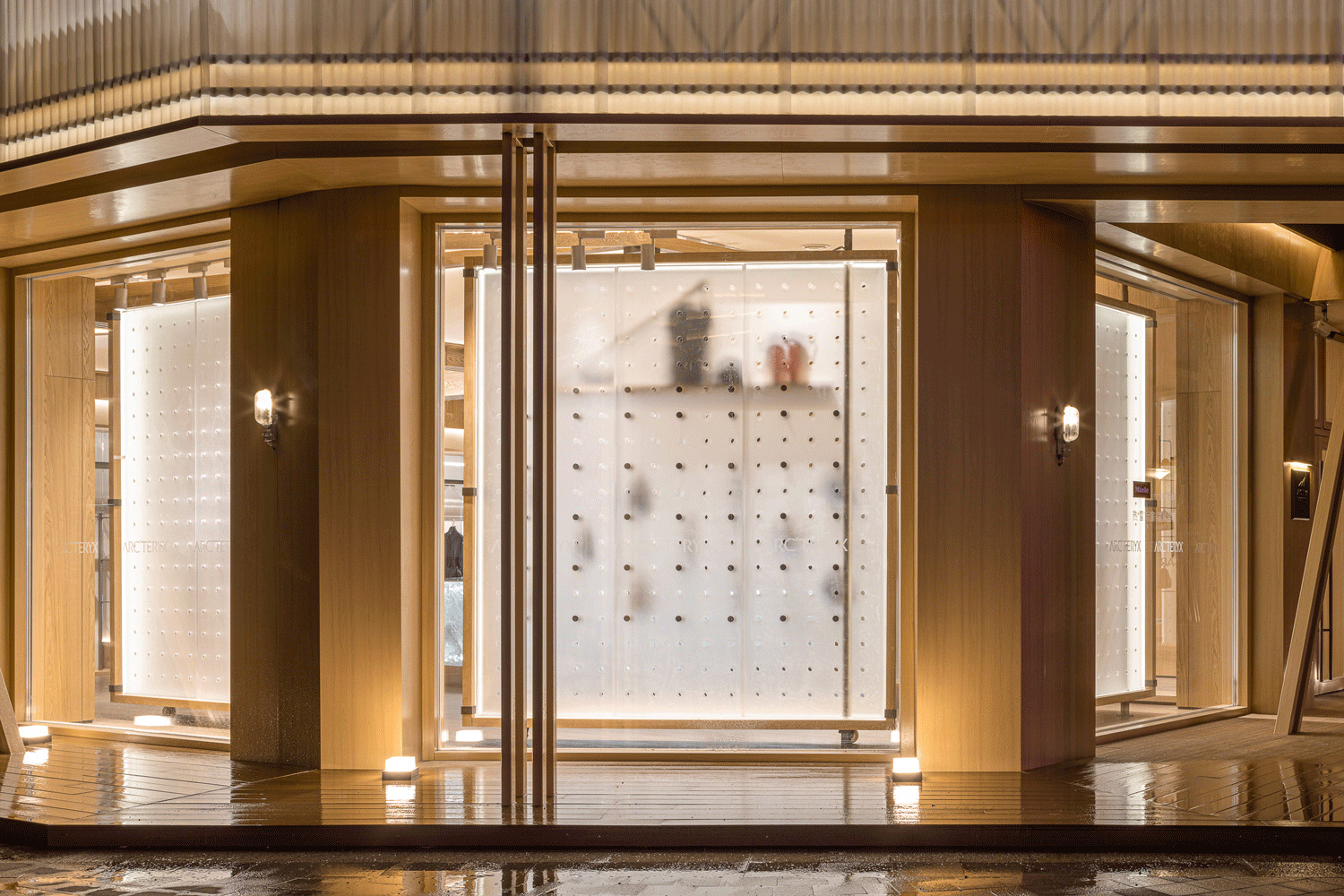 White studded panel behind glass storefront with figures moving past at night
