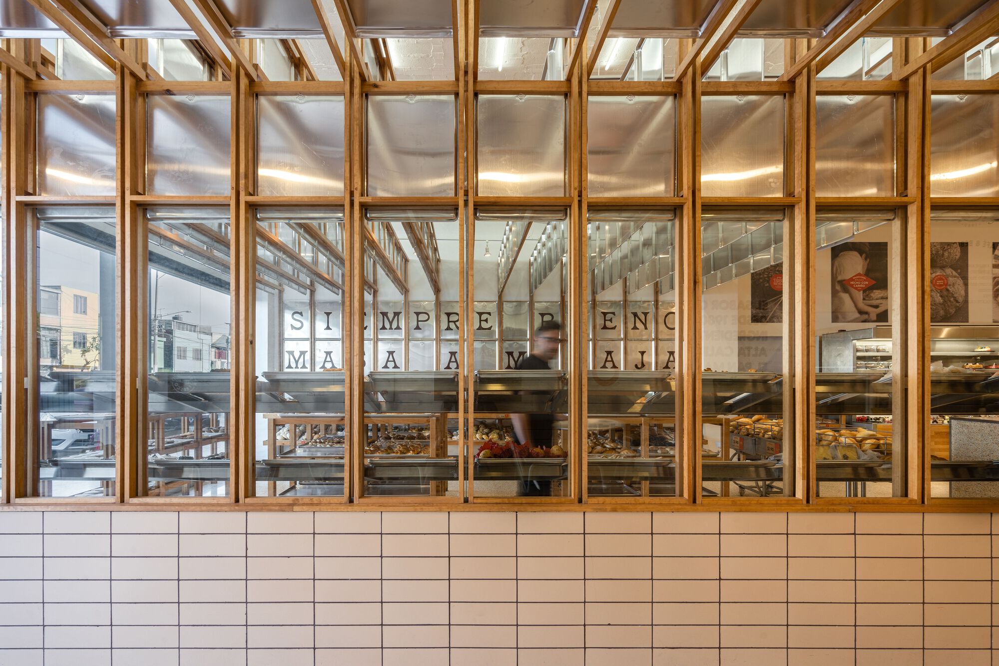 Street view through timber and glass storefront with white tile base and baked goods on display