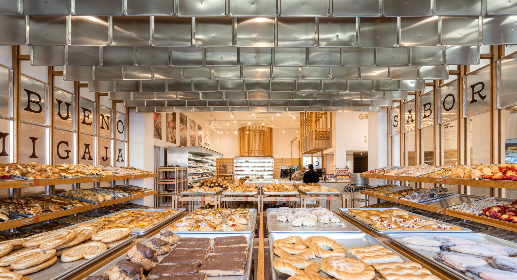 View through the bakery showing timber trays of pastries beneath a woven metal ceiling installation
