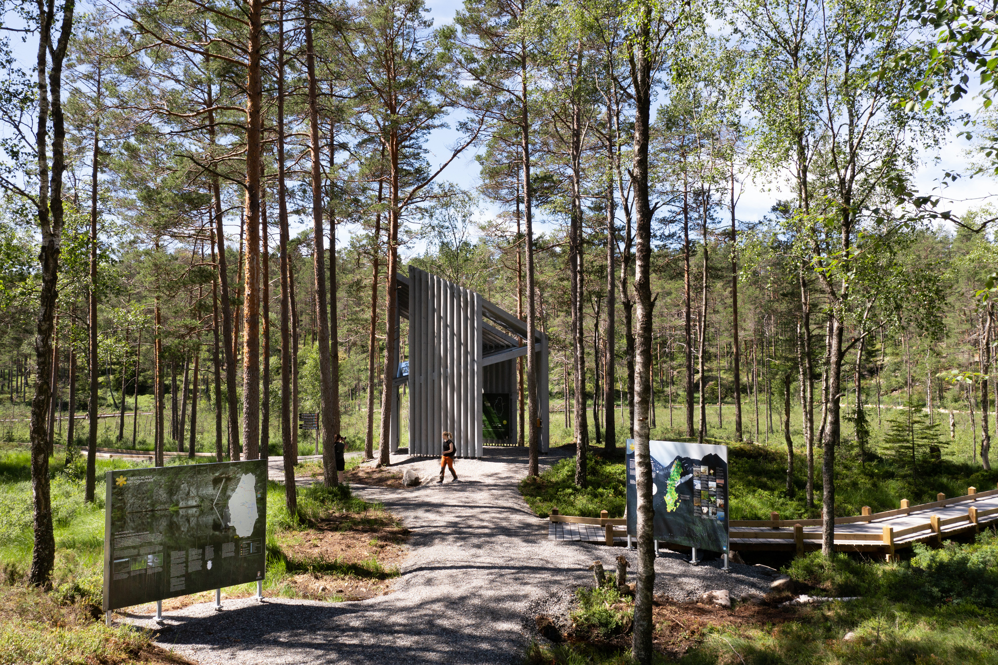 Gravel path leading to a vertical timber slatted chapel set among tall pine trees