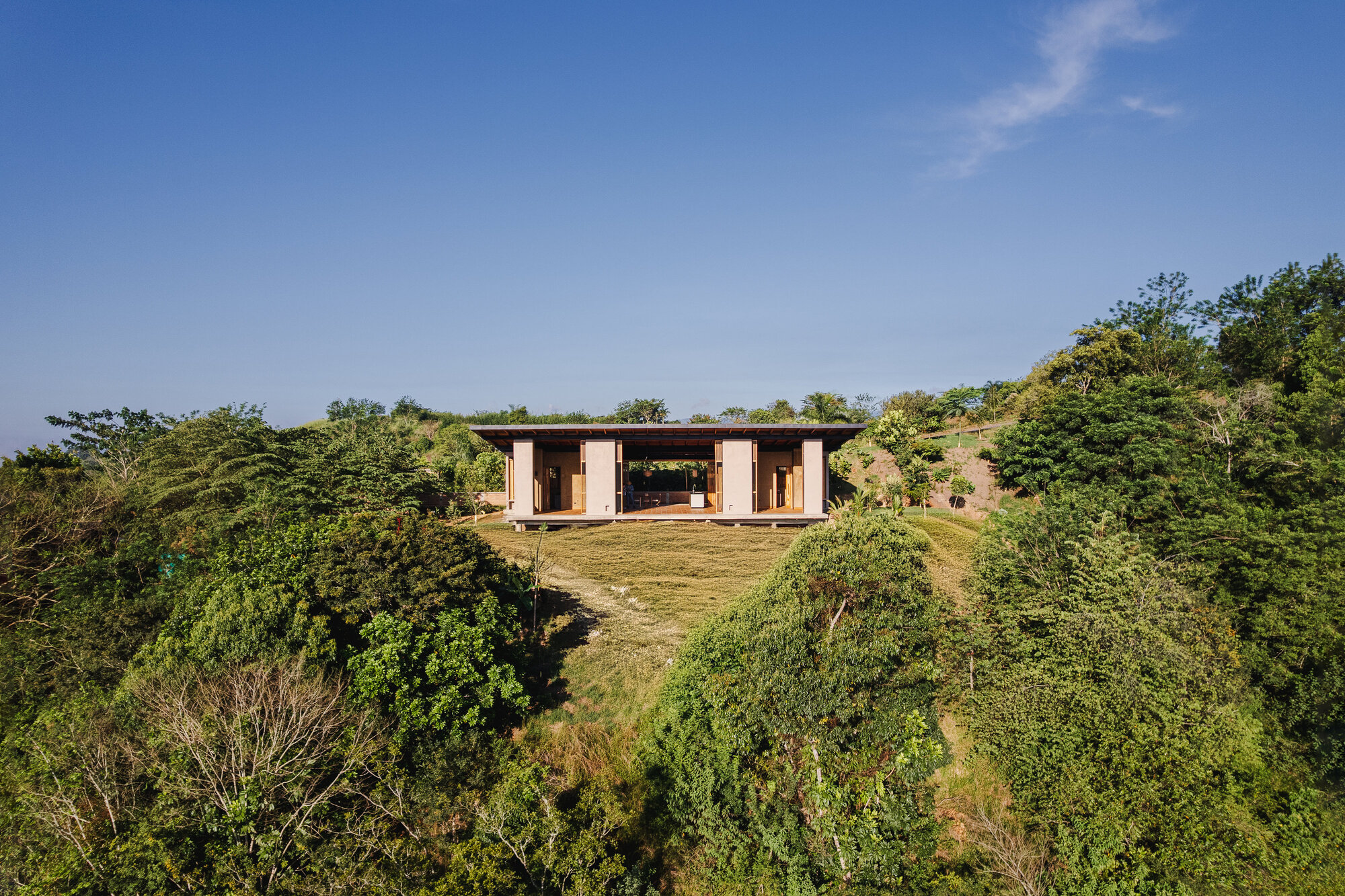 Hillside pavilion with timber volumes nestled into lush green slopes under clear blue sky