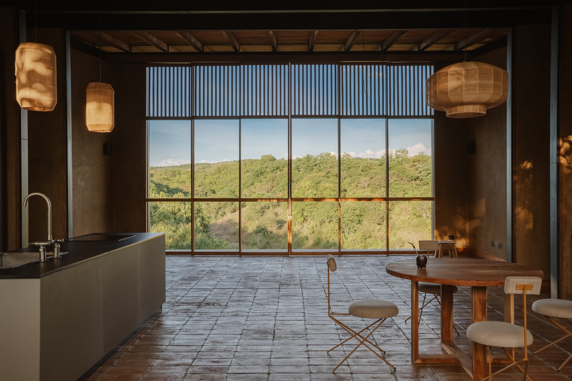 Living area with floor-to-ceiling steel-framed windows, timber louvered screen above, and woven pendant lights hanging from ceiling