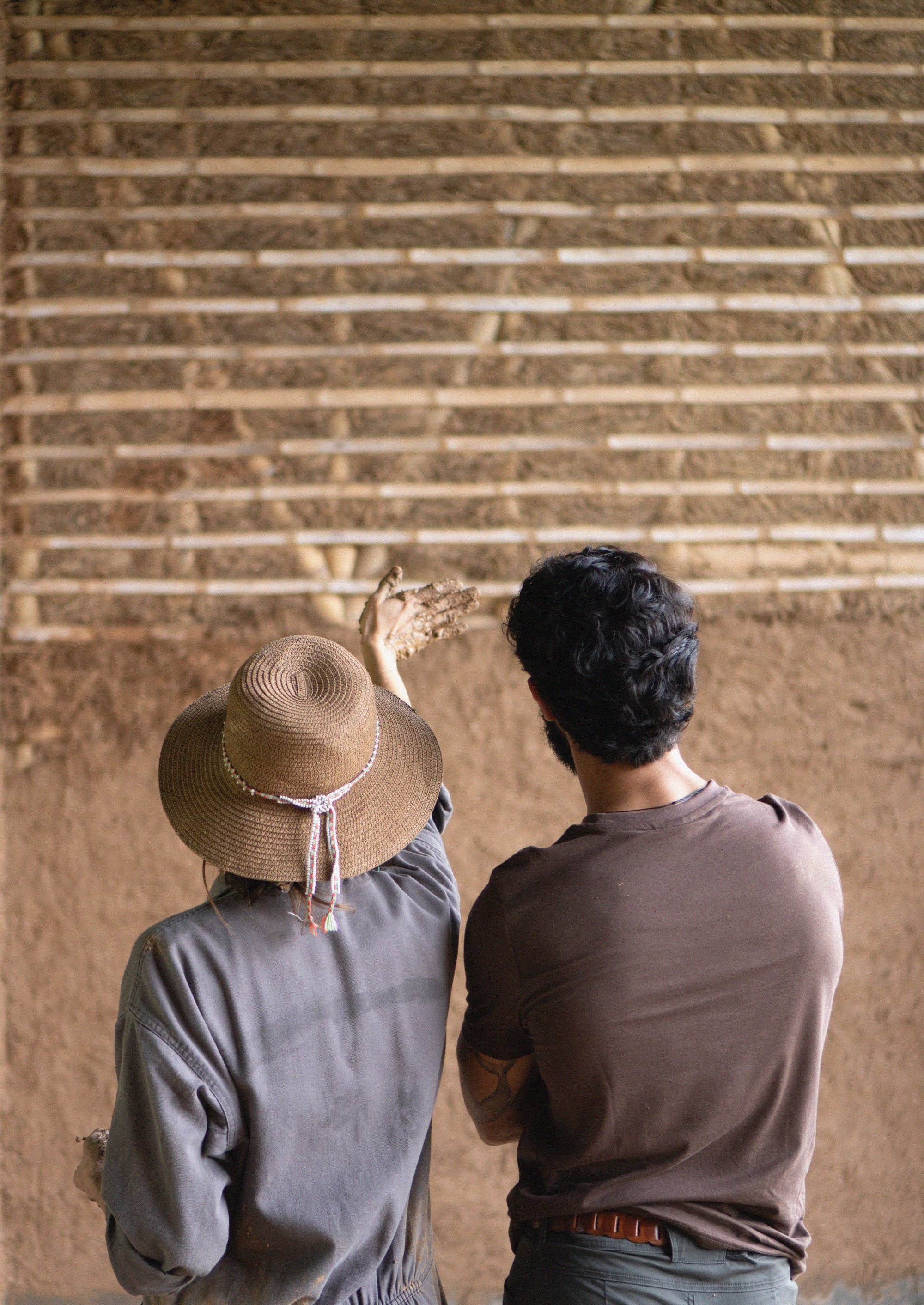 Two workers applying clay plaster by hand to horizontal bamboo lath wall structure