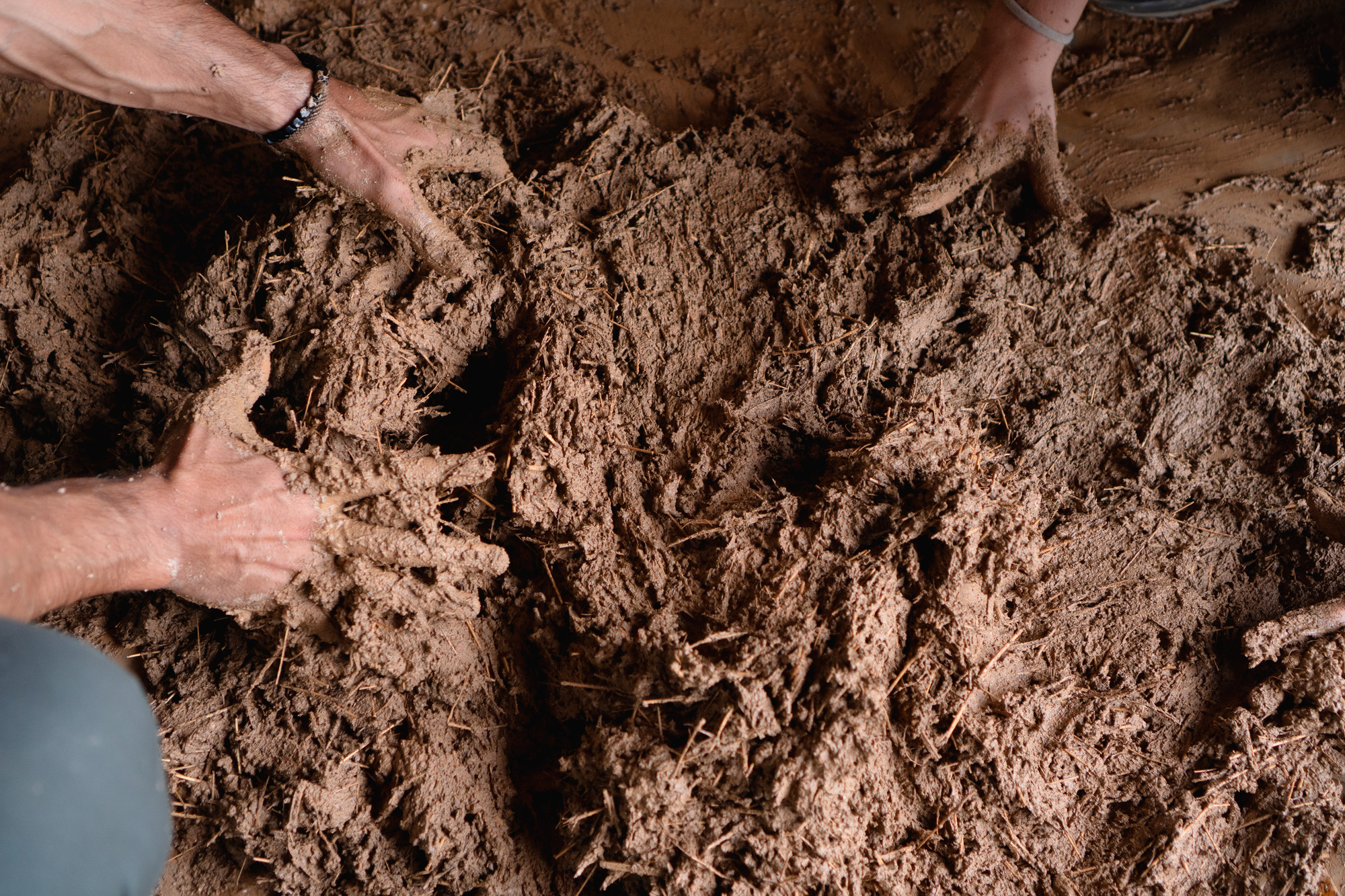 Hands mixing wet clay and straw composite material for wall infill
