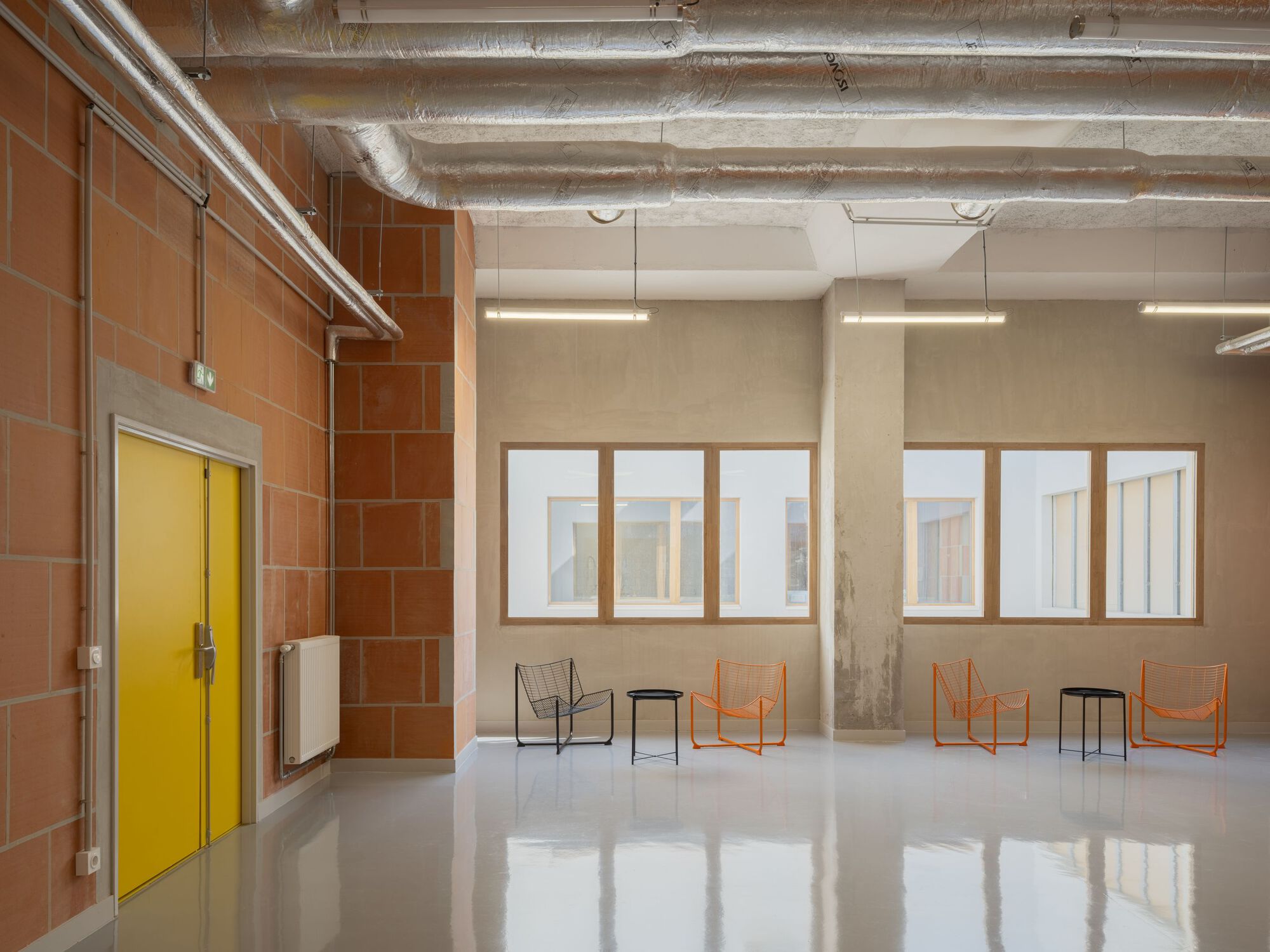 Interior hall with terracotta tile wall, yellow door, exposed concrete ceiling and polished white floor