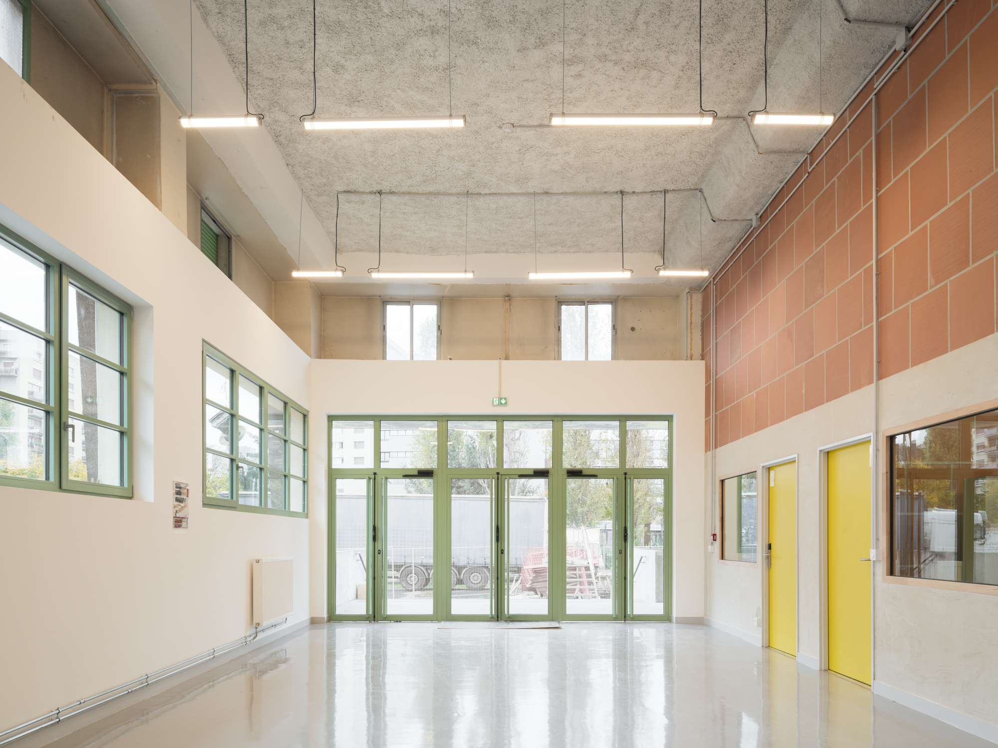 Double-height entrance hall with green glazed doors, exposed concrete ceiling and suspended linear lighting