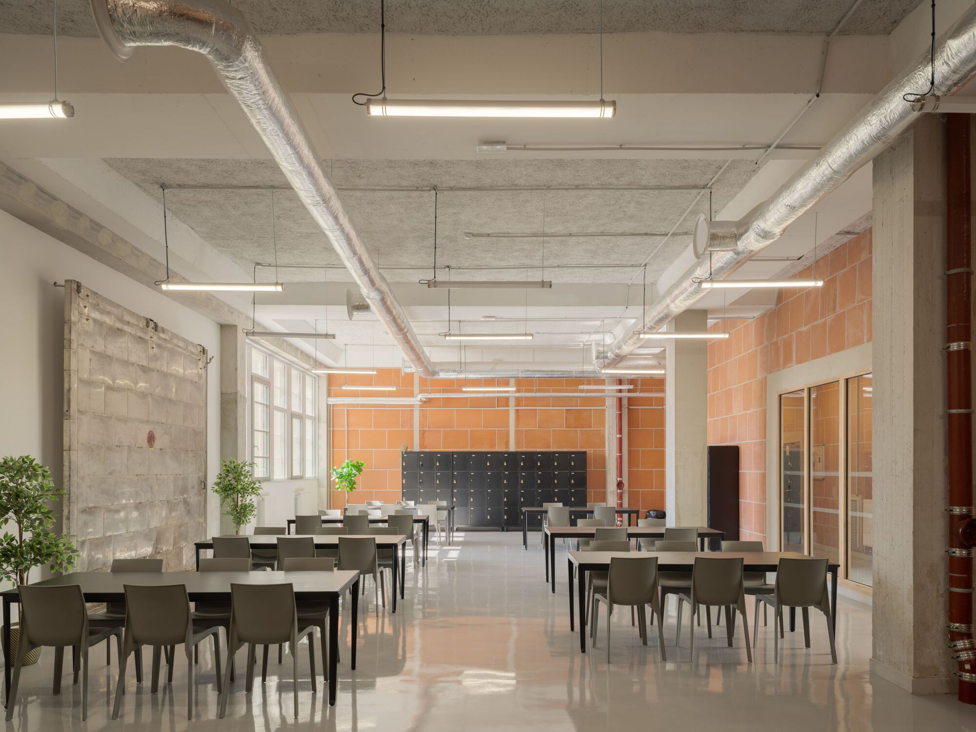 Dining hall with exposed ductwork, concrete columns, terracotta tile walls and rows of tables
