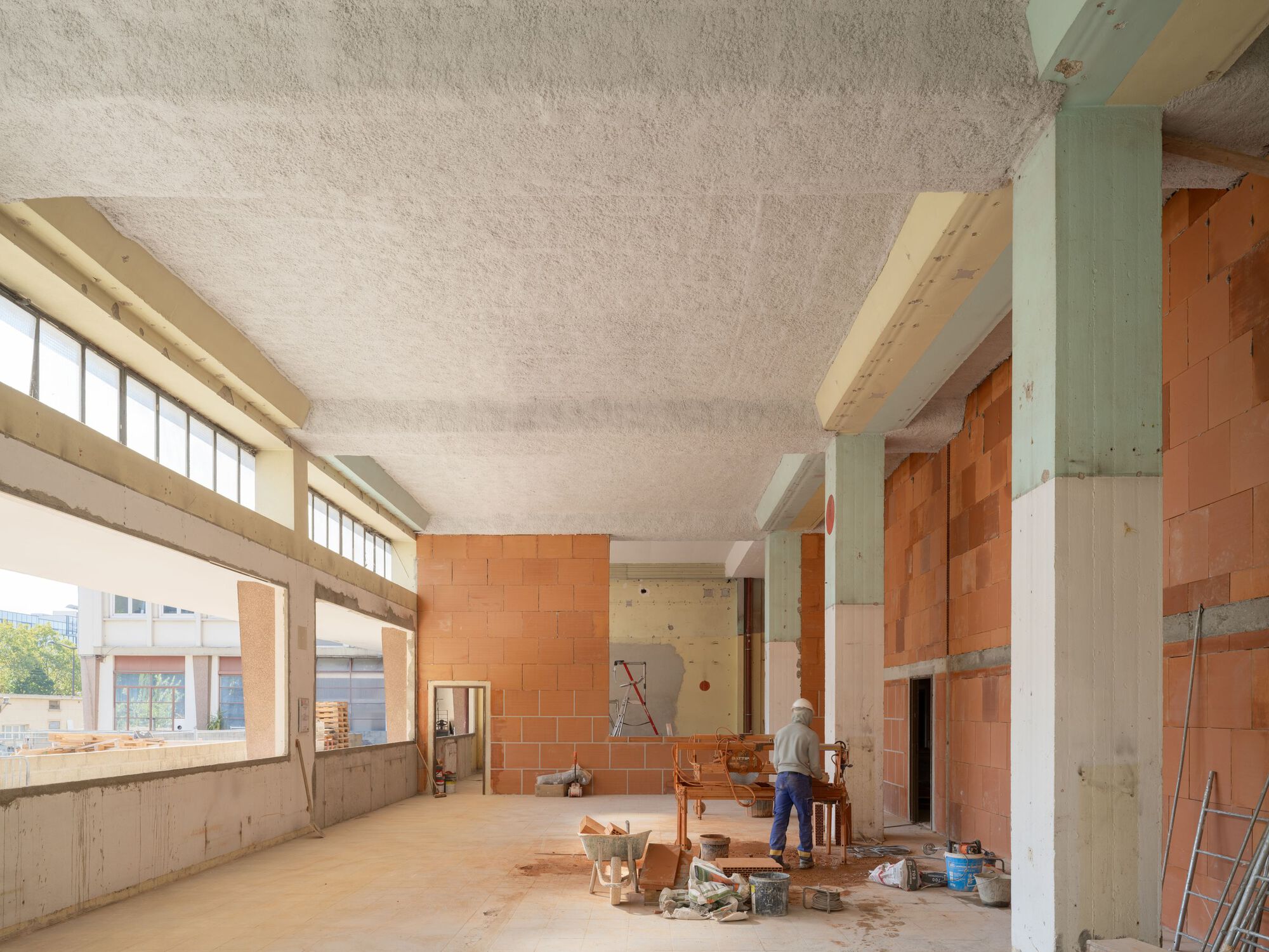Construction site interior with timber beams, concrete ceiling, terracotta block walls, and worker amid building materials