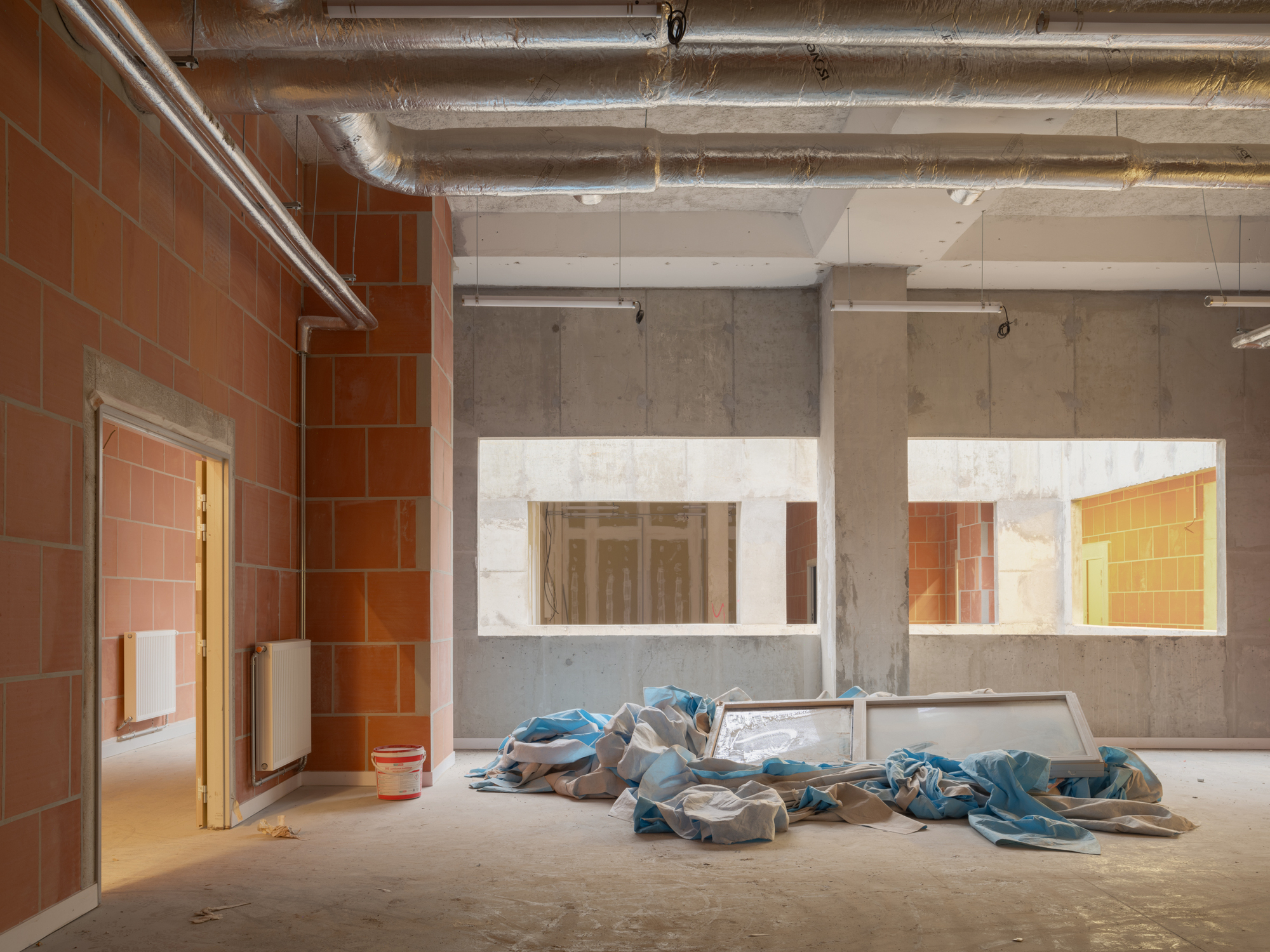 Unfinished interior space with terracotta tile walls, concrete partitions, exposed ductwork, and construction debris on floor