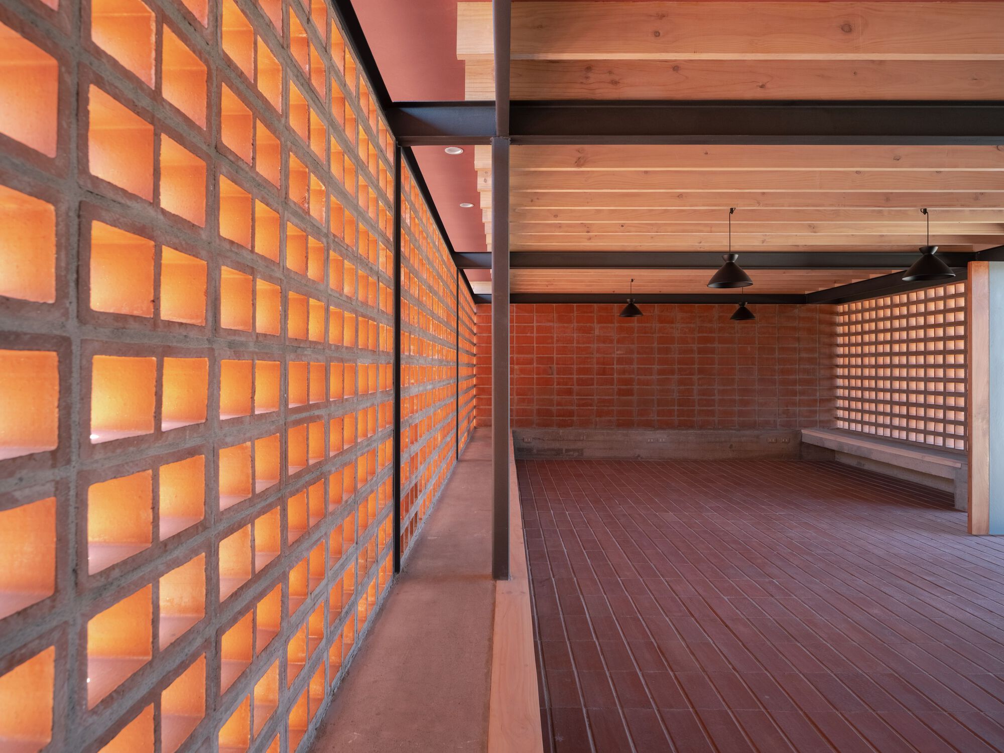 Interior space with backlit terracotta block screen walls and exposed timber ceiling at dusk
