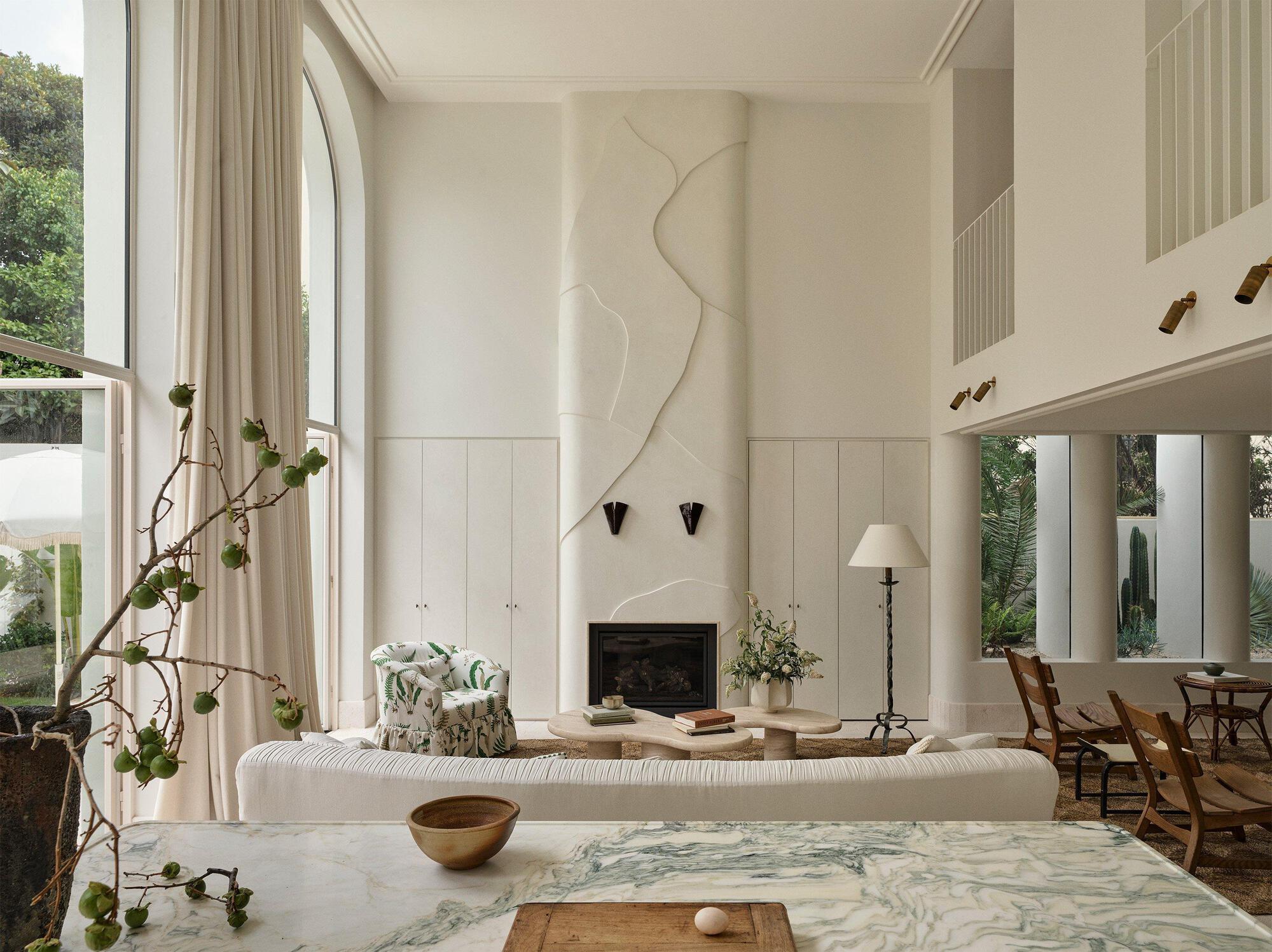 Double-height living room with arched windows, fireplace, and marble-topped central table