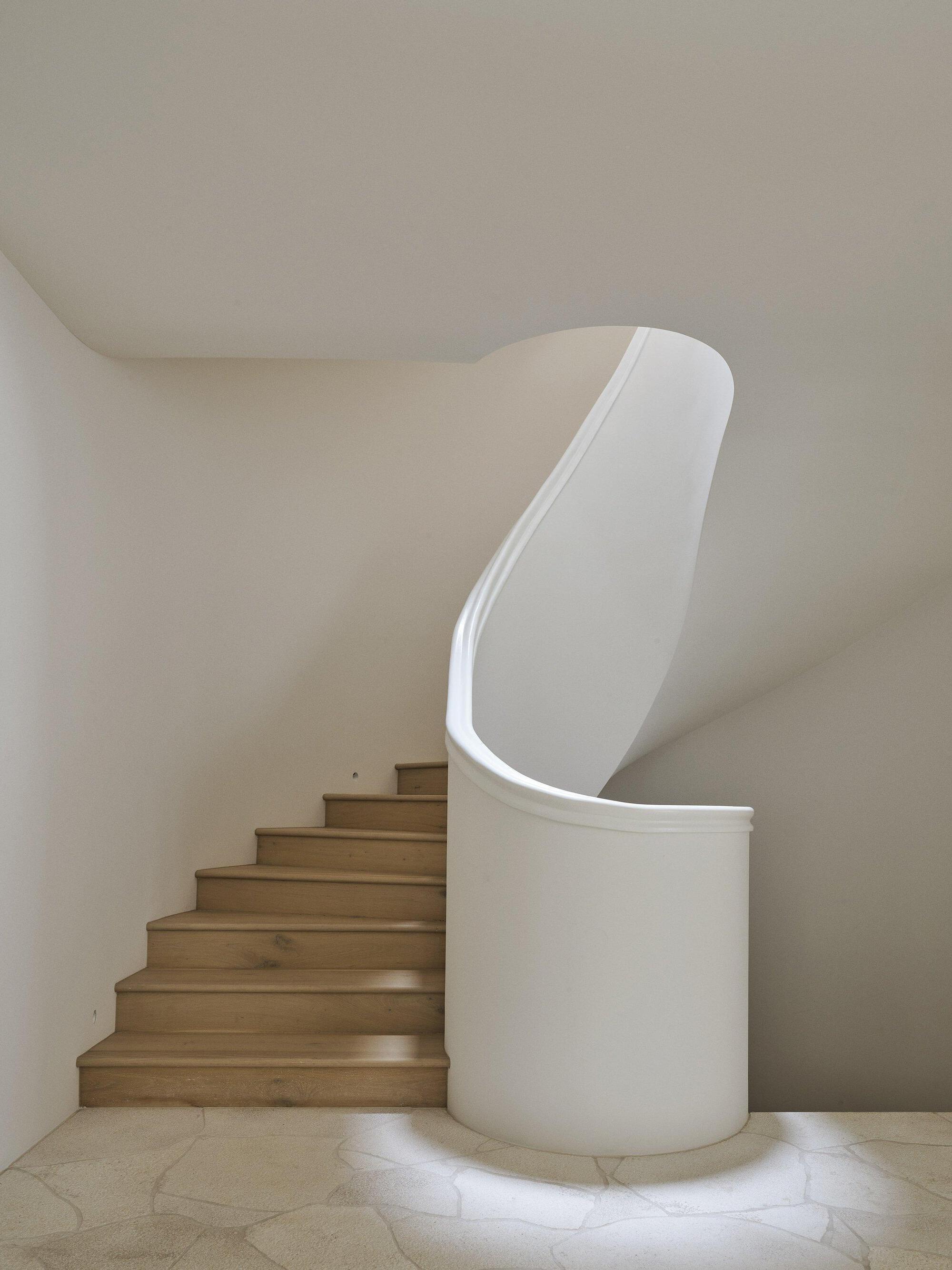 Curved timber staircase with white cylindrical base and sculptural opening above the landing