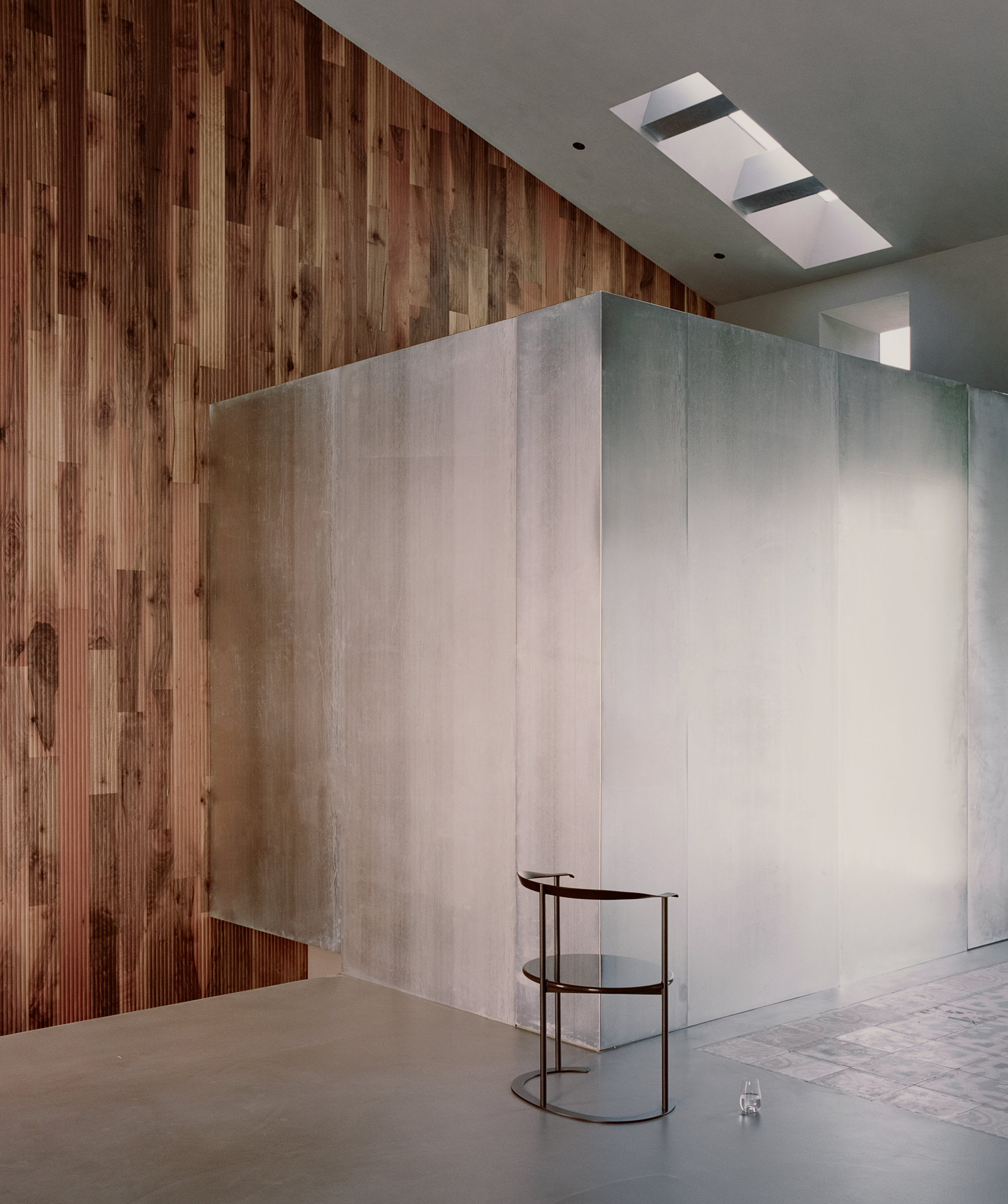 Freestanding volume clad in pale panels beside vertical timber wall with skylight above