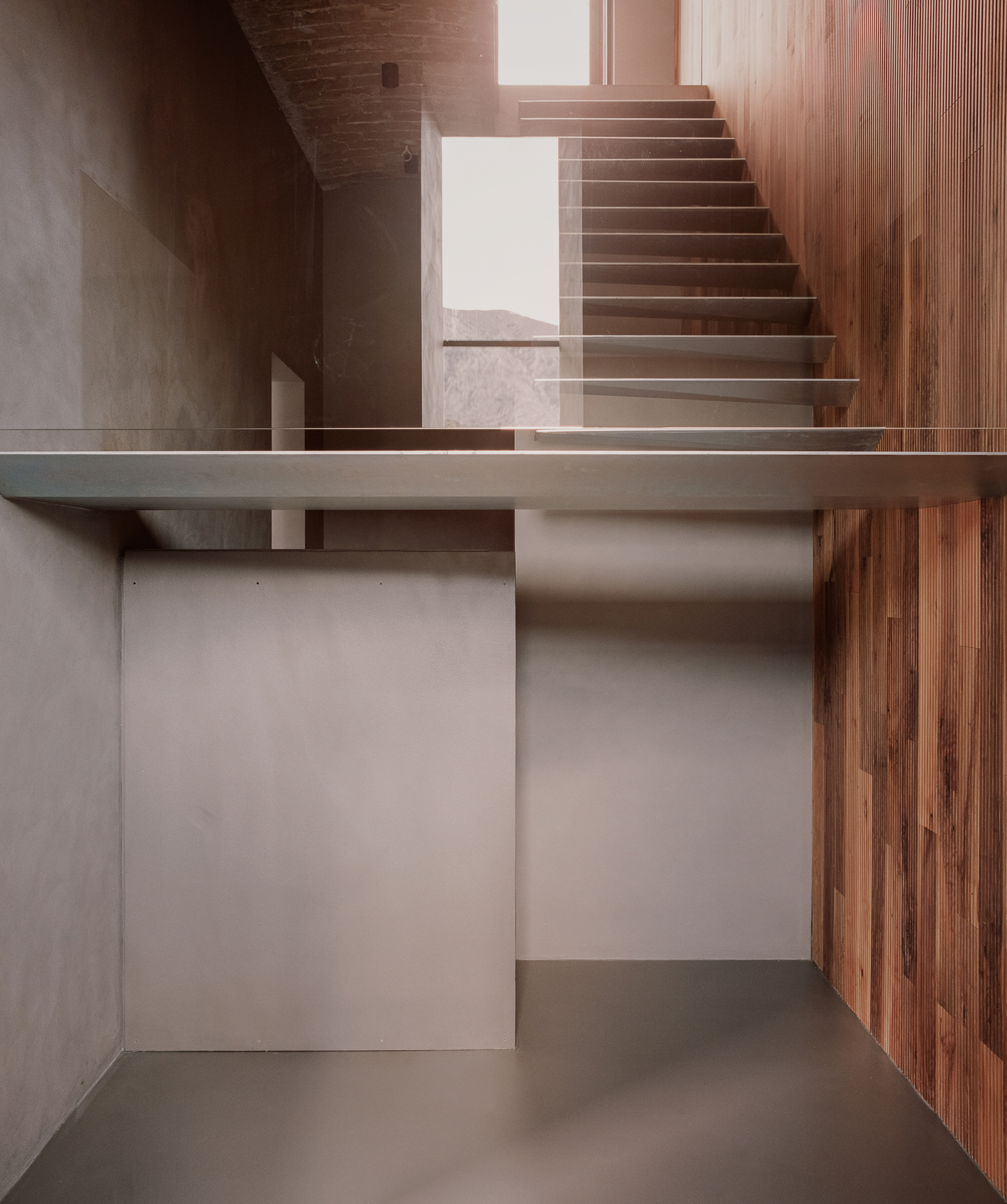 Double-height space showing timber staircase rising beside a mezzanine landing with rendered walls