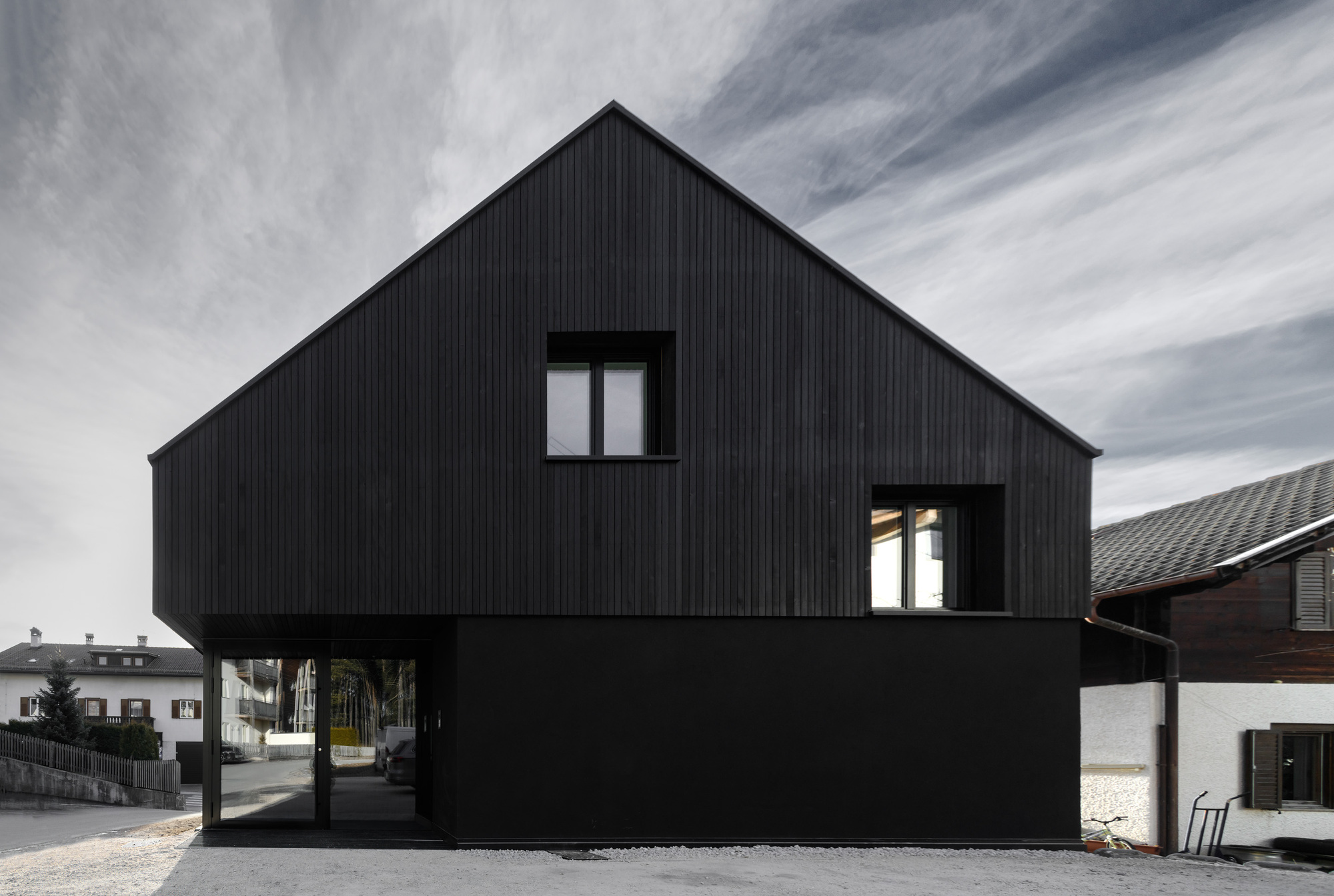 Blackened wood facade with upper volume cantilevered over open ground floor supported by recessed columns