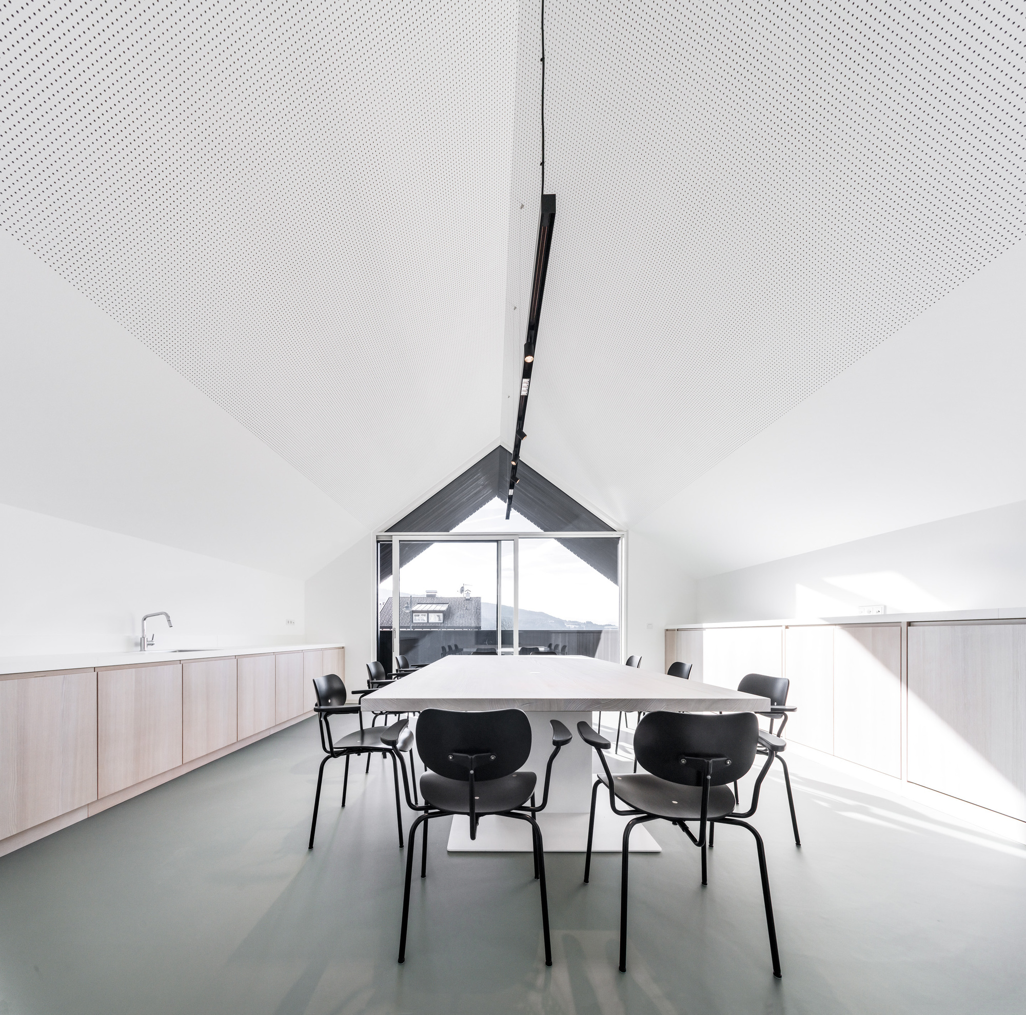 Vaulted dining space with perforated acoustic ceiling panels and gable window framing mountain view beyond
