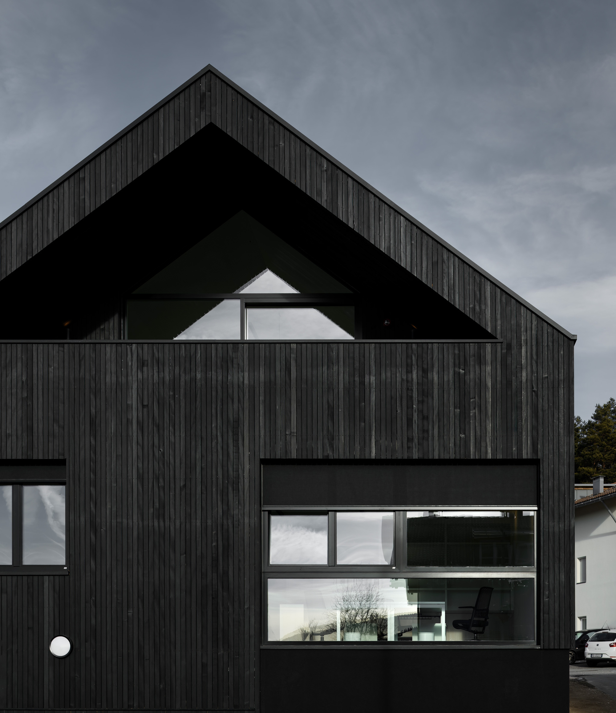 Gable end with triangular upper window above ribbon glazing revealing interior spaces at dusk